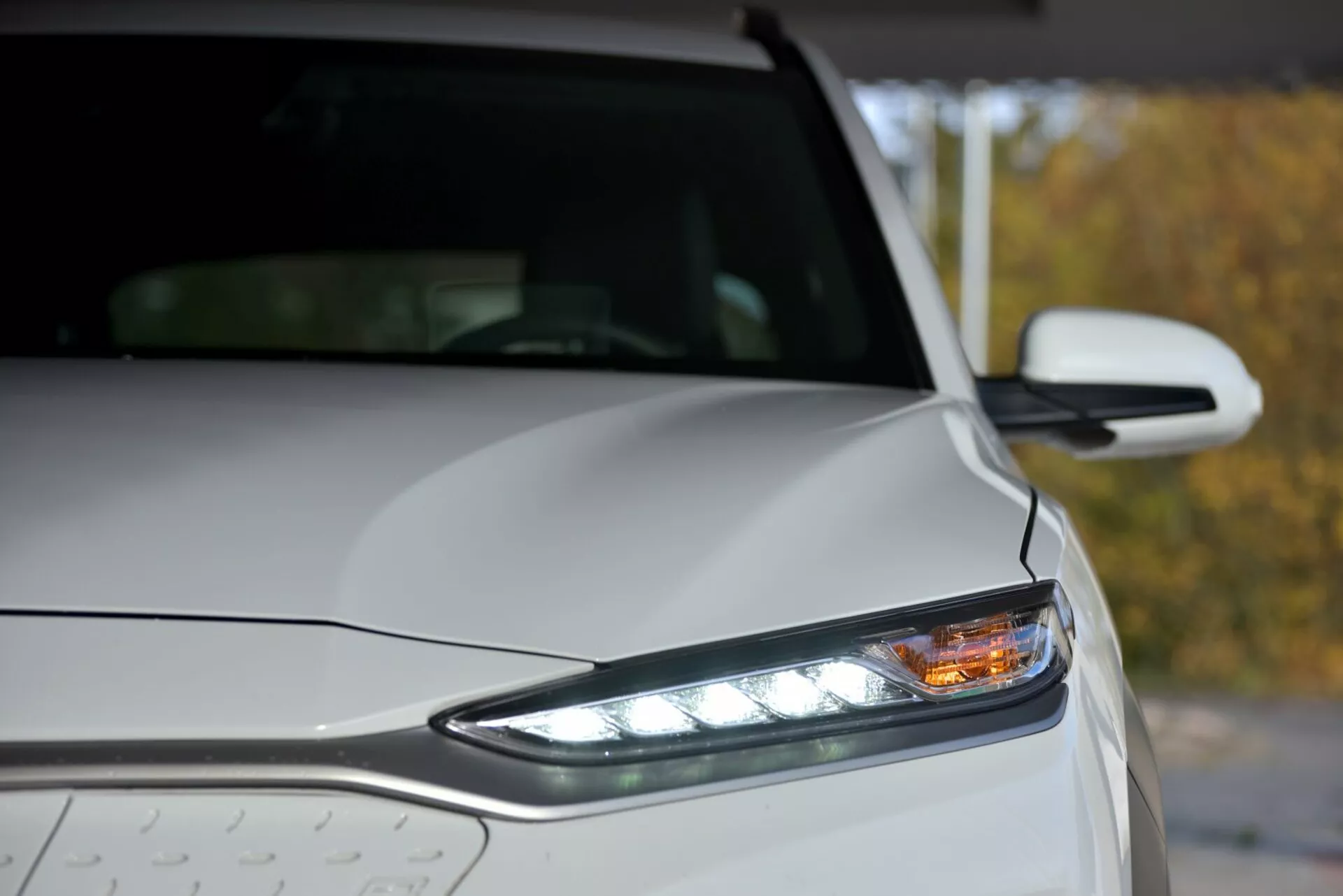 Close-up di Hyundai Kona Elektro 2021 con faro anteriore sinistro LED, luci diurne e gocce di pioggia sulla carrozzeria metallica