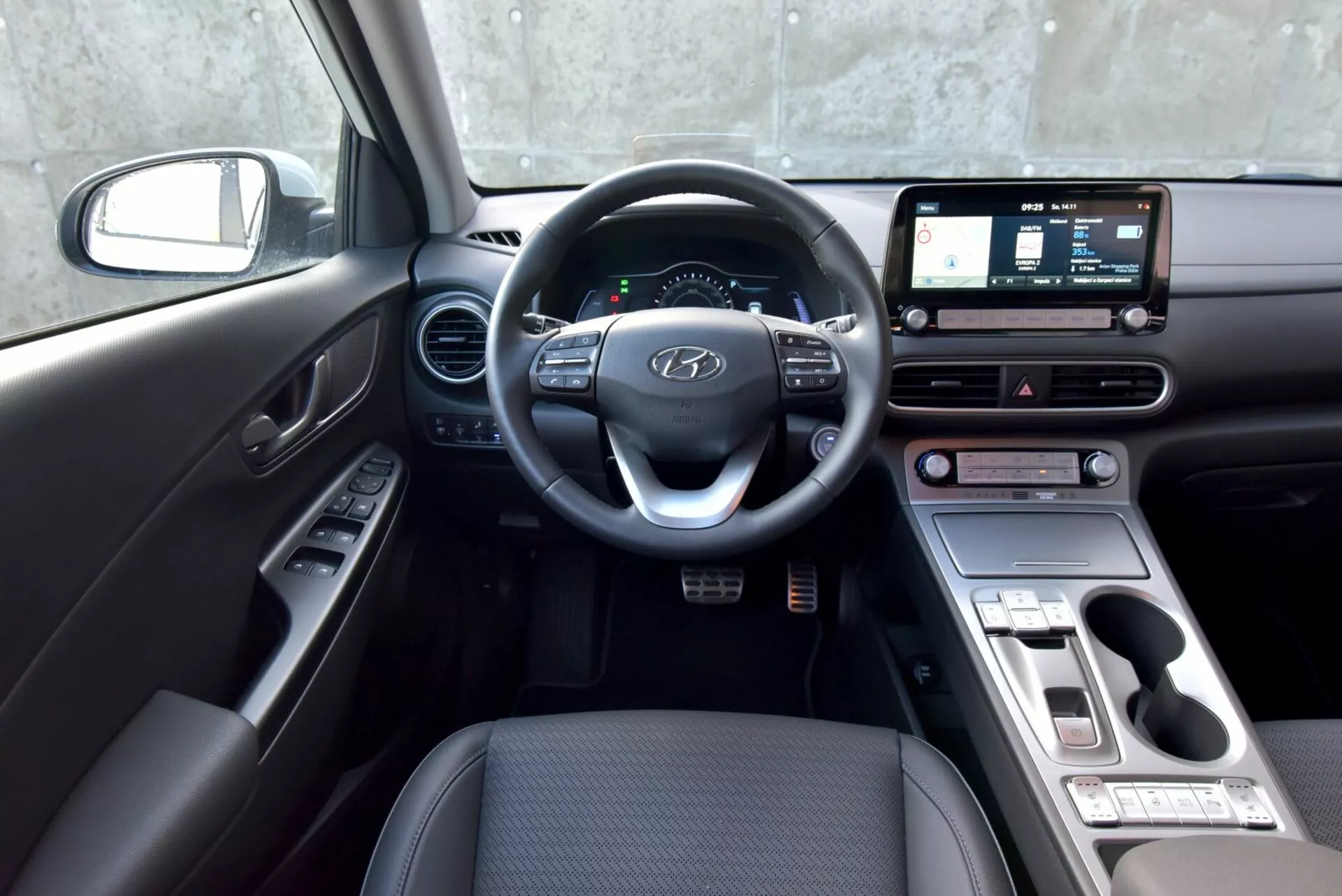 Interni della Hyundai Kona Elettrica 2021 dalla prospettiva del lato conducente con volante, cruscotto, touchscreen dell'infotainment, comandi per la climatizzazione e selettore del cambio