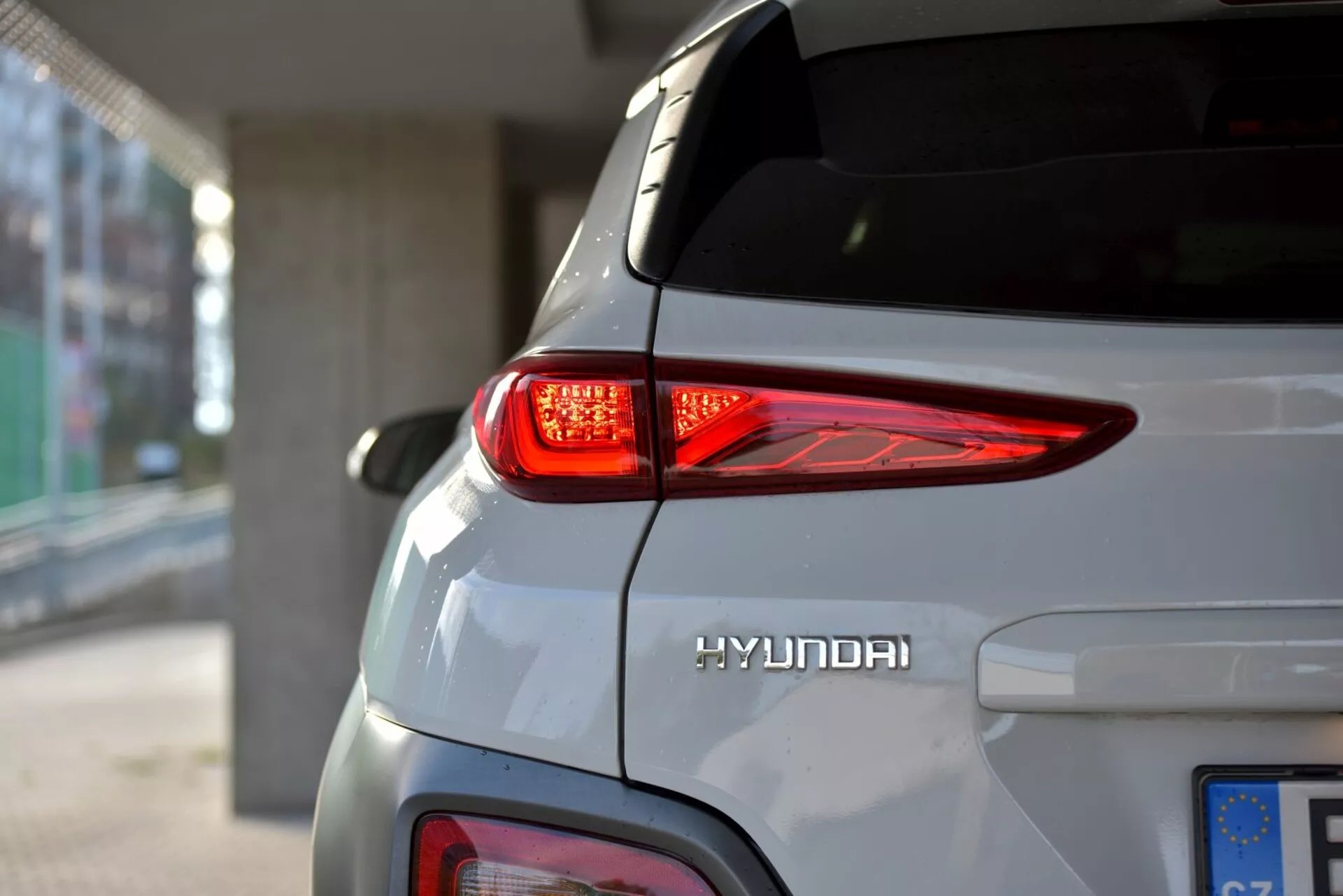 Vista ravvicinata del lato destro posteriore di una Hyundai Kona Elettrica 2021, con in evidenza la luce posteriore LED curva, il logo Hyundai e la carrozzeria elegante di colore argento sotto l'illuminazione naturale