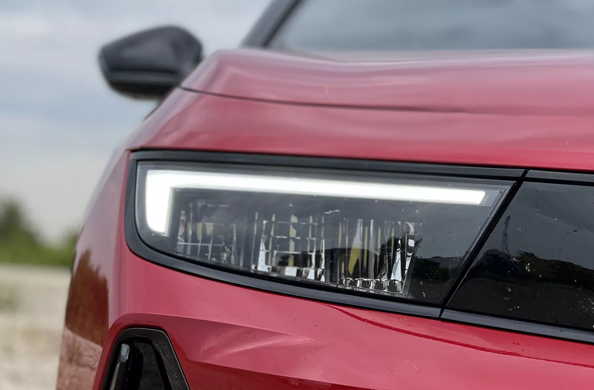 Primo piano laterale frontale di una Opel Astra rossa 2022 che mette in evidenza il design dettagliato del faro LED, dimostrando la tecnologia di illuminazione moderna e i contorni del veicolo