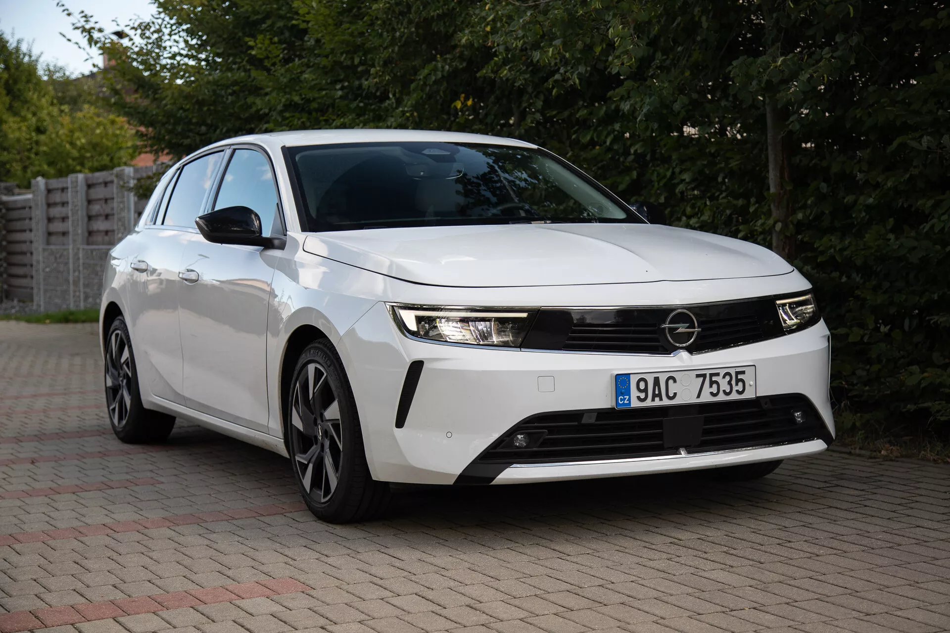 Opel Astra 2022 catturata in un contesto suburbano, mettendo in mostra i suoi fari eleganti, la griglia frontale prominente, il design aerodinamico comprese le ruote in lega a più razze, e la tecnologia innovativa da una vista frontale di tre quarti