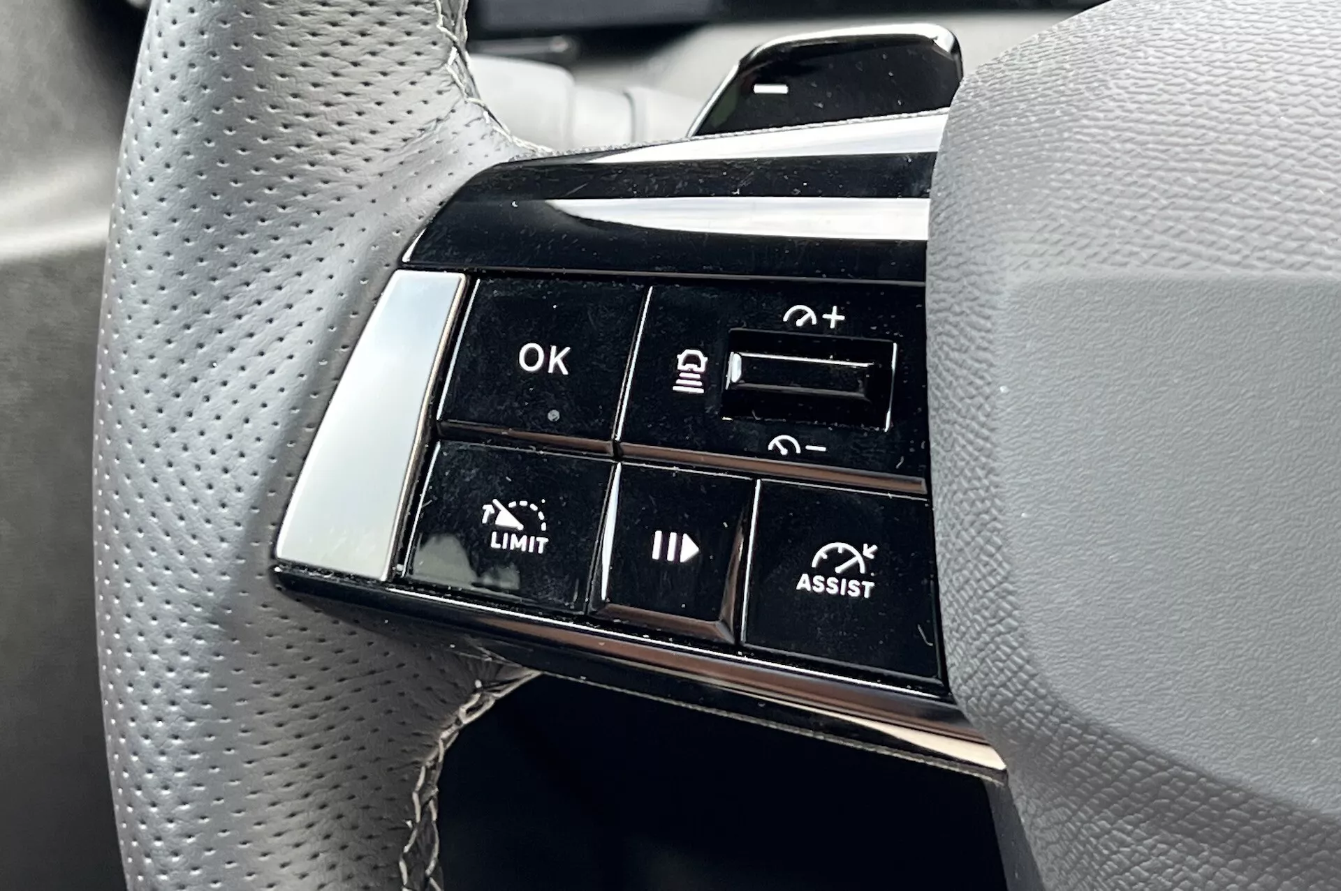 Primo piano del cluster di pulsanti sul volante della Opel Astra 2022 che evidenzia le caratteristiche avanzate di assistenza alla guida, inclusi il controllo della velocità adattivo e l'assistenza al mantenimento della corsia, con un focus sulle etichette funzionali come OK, +, -, LIMIT e ASSIST dalla prospettiva del guidatore