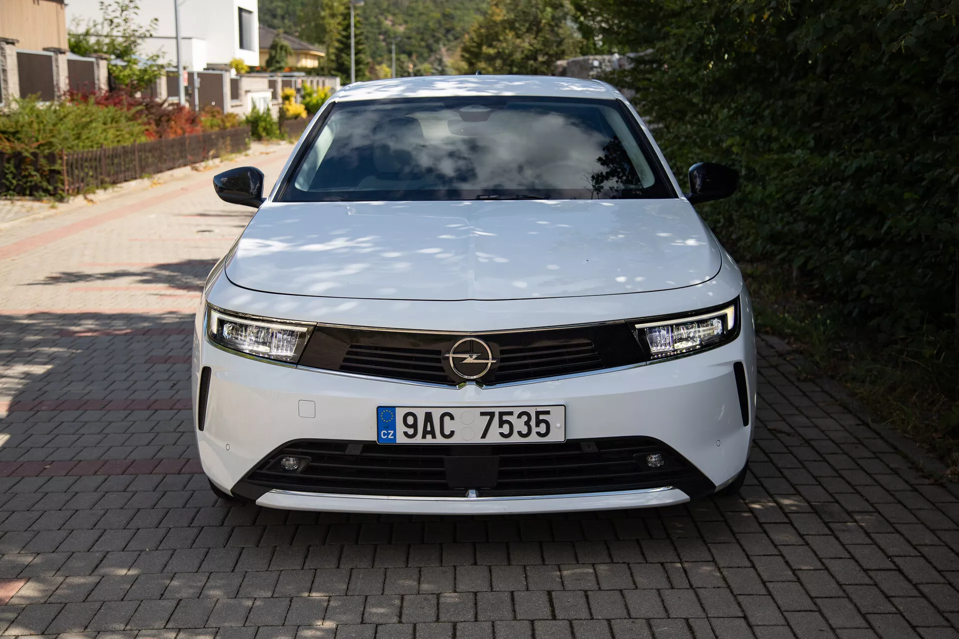 Vista frontale dell'Opel Astra 2022 che mostra un design moderno di veicolo elettrico con fari LED, griglia decorativa e forma aerodinamica, parcheggiato in un vialetto residenziale