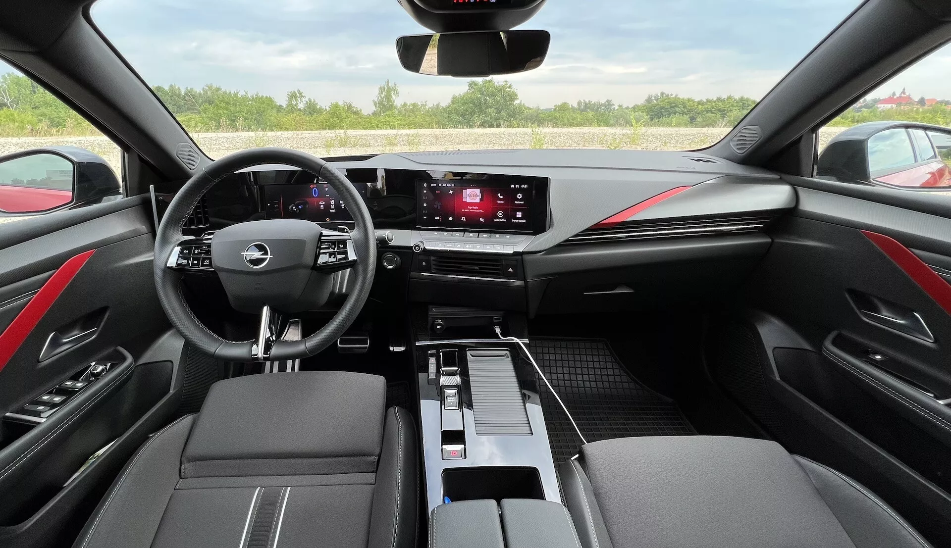 Interni Opel Astra 2022 con volante multifunzione a tre razze, cruscotto digitale, sistema di infotainment touchscreen, comandi climatizzatore eleganti, finiture in pelle bicolore con cuciture rosse e design moderno dell'abitacolo dal punto di vista del conducente