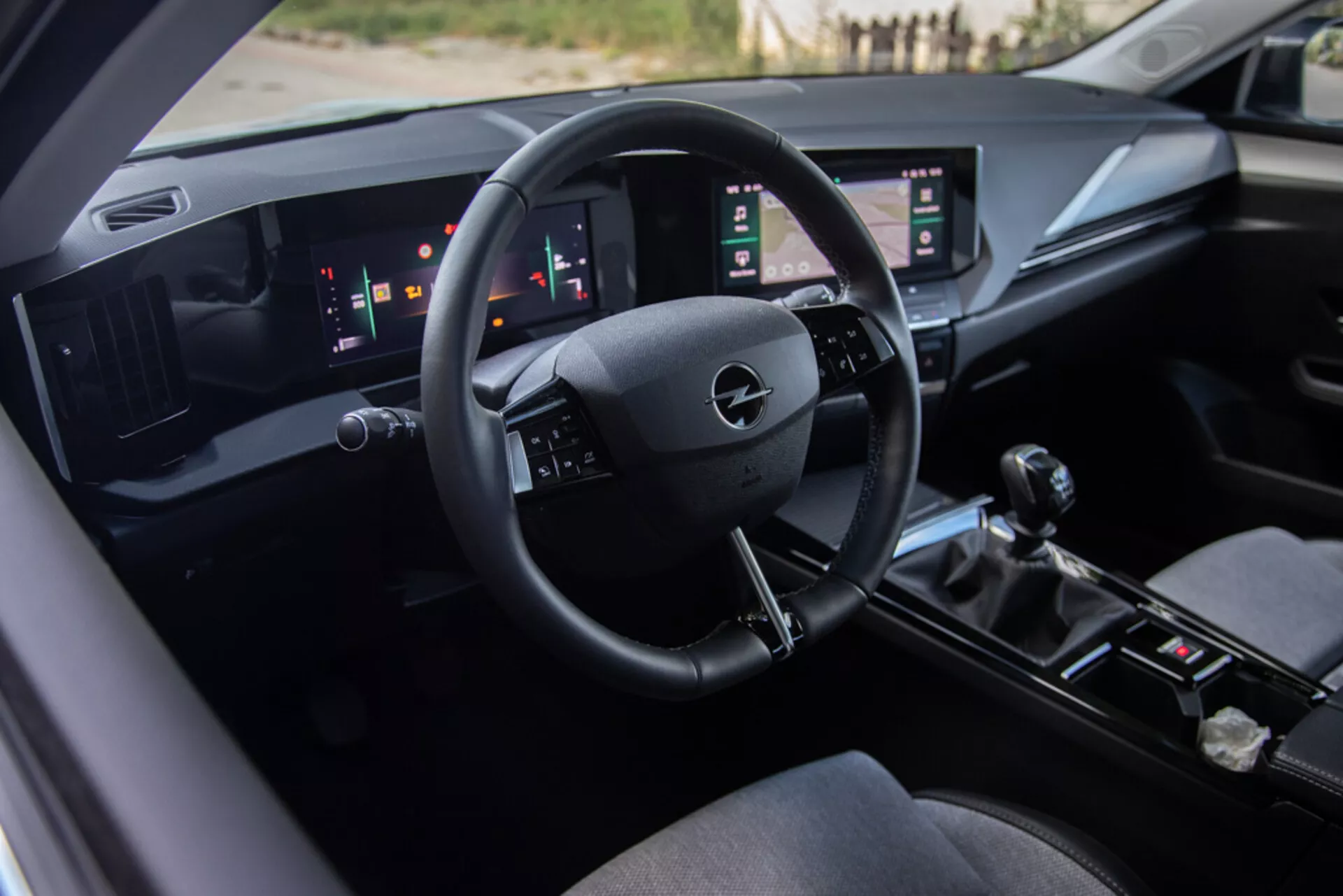 Interni Opel Astra 2022 con sedile del conducente, cruscotto tecnologicamente avanzato con logo Opel sul volante, indicatori digitali e doppio pannello touchscreen verticale