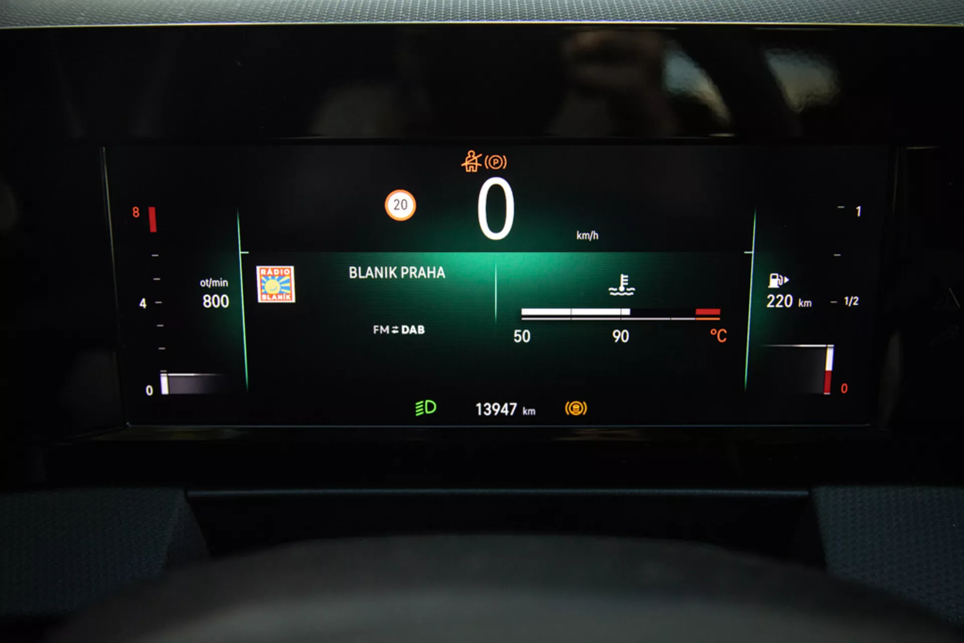 Vista del cruscotto digitale della Opel Astra 2022 che evidenzia il quadro strumenti con RPM, livello batteria, tachimetro, indicatore carburante, temperatura esterna, stazione radio 'BLANIK PRAHA', e lettura dell'odometro dalla prospettiva del sedile del conducente.