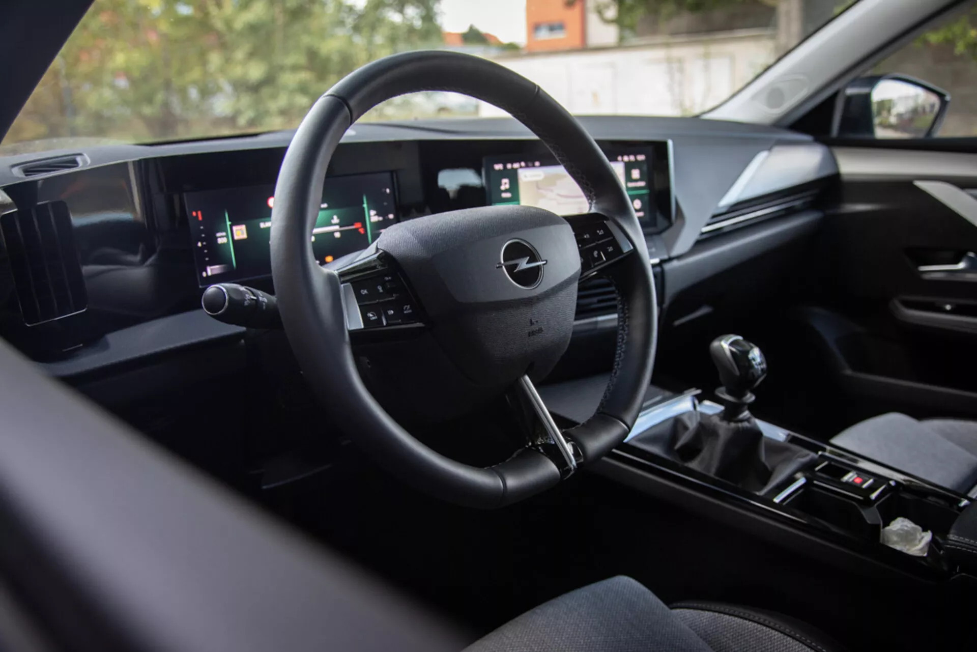 Interno Opel Astra 2022 che mostra la moderna tecnologia del cruscotto digitale, volante multifunzione, sistema di infotainment a doppio schermo largo e leva del cambio manuale per prestazioni sportive, vista dal sedile posteriore verso l'area del conducente con finiture premium