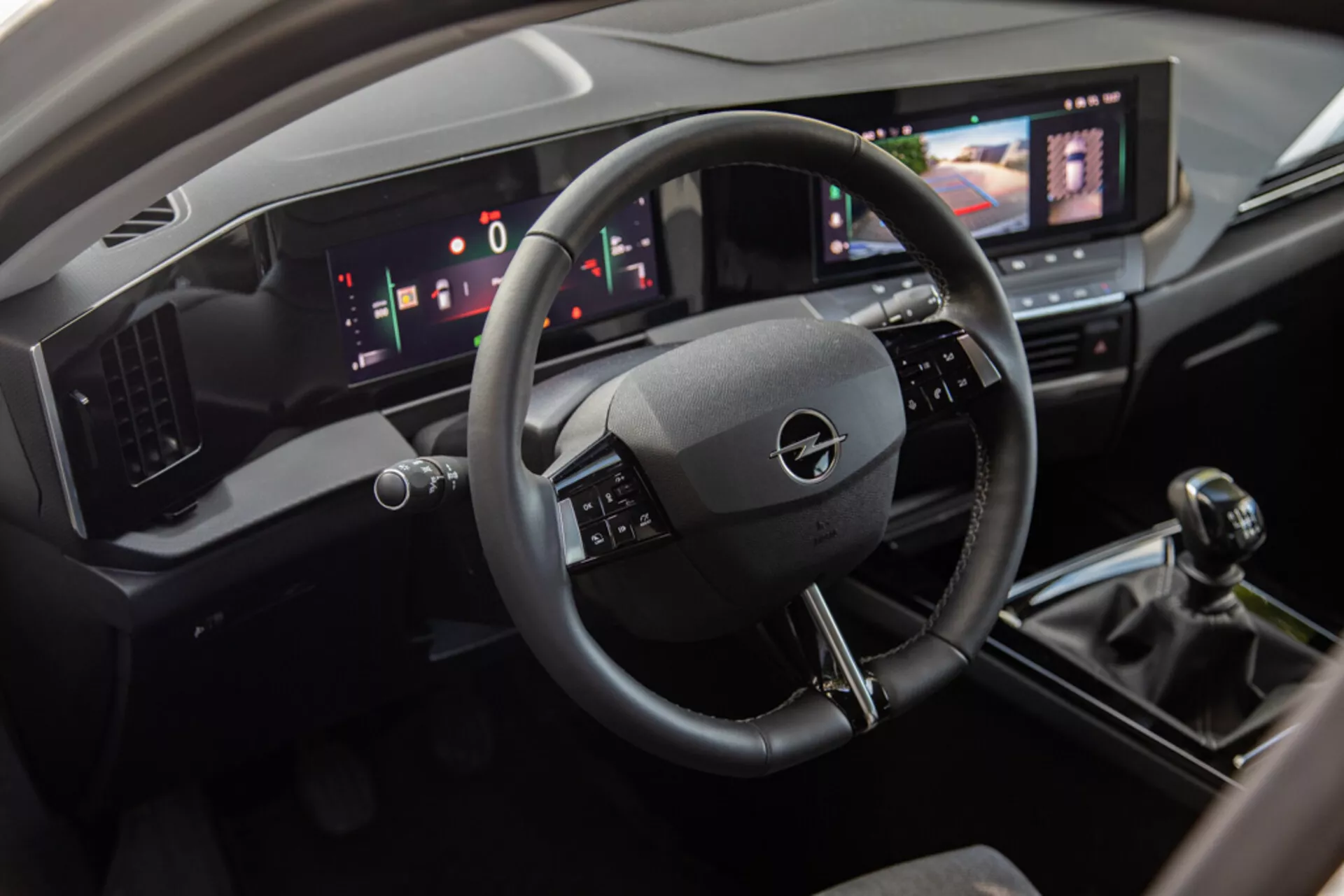 Vista interna dell'Opel Astra 2022 che mostra l'area del conducente con volante a tre razze, cruscotto digitale e console centrale inclusa un sistema di infotainment touchscreen, cambio manuale e comandi moderni per il clima