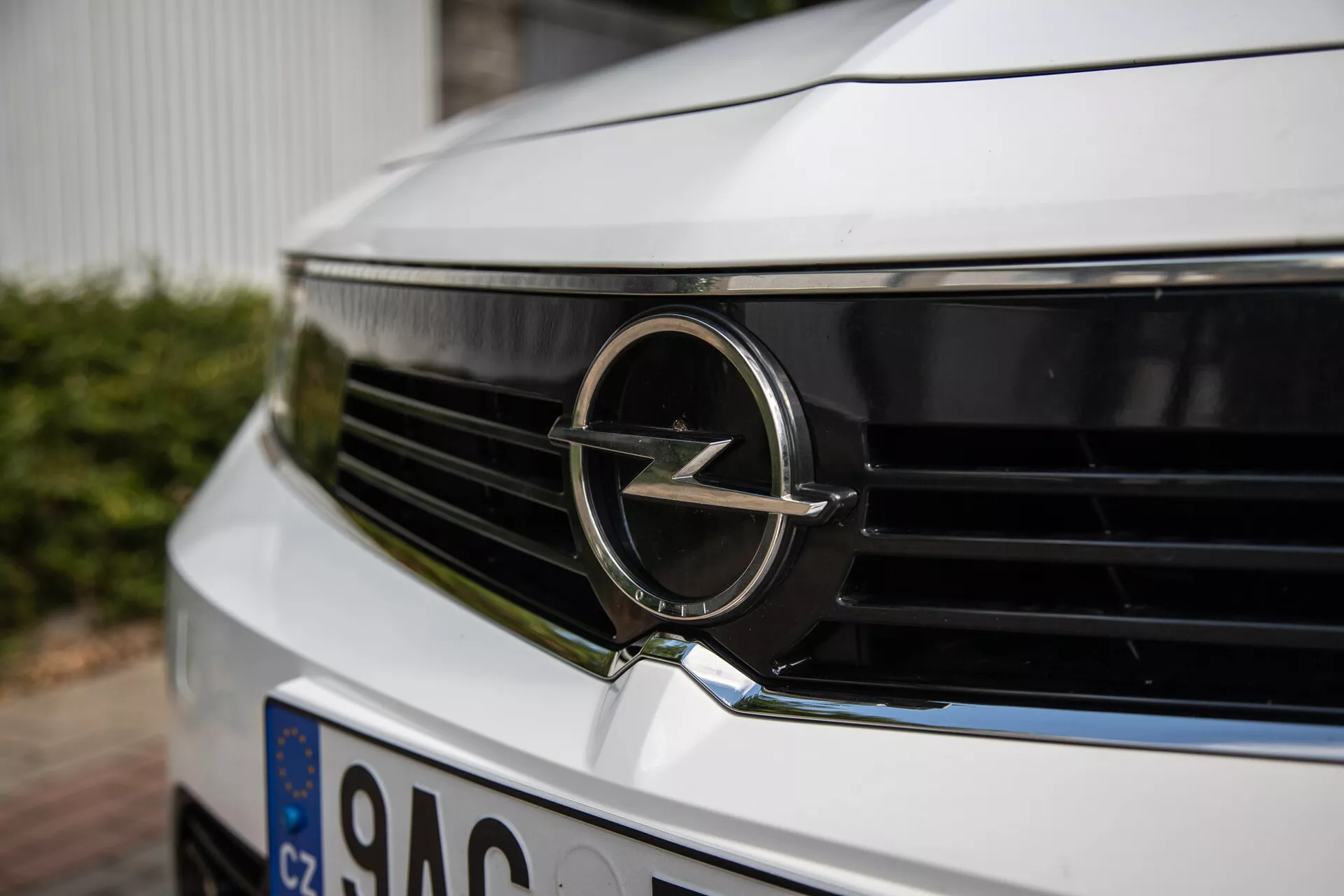 Primo piano della griglia anteriore e del badge Opel su un modello 2022, evidenziando il dettaglio dell'emblema e il design delle lamelle orizzontali da un angolo basso e leggermente decentrato, mettendo in luce l'estetica contemporanea e l'identità del marchio