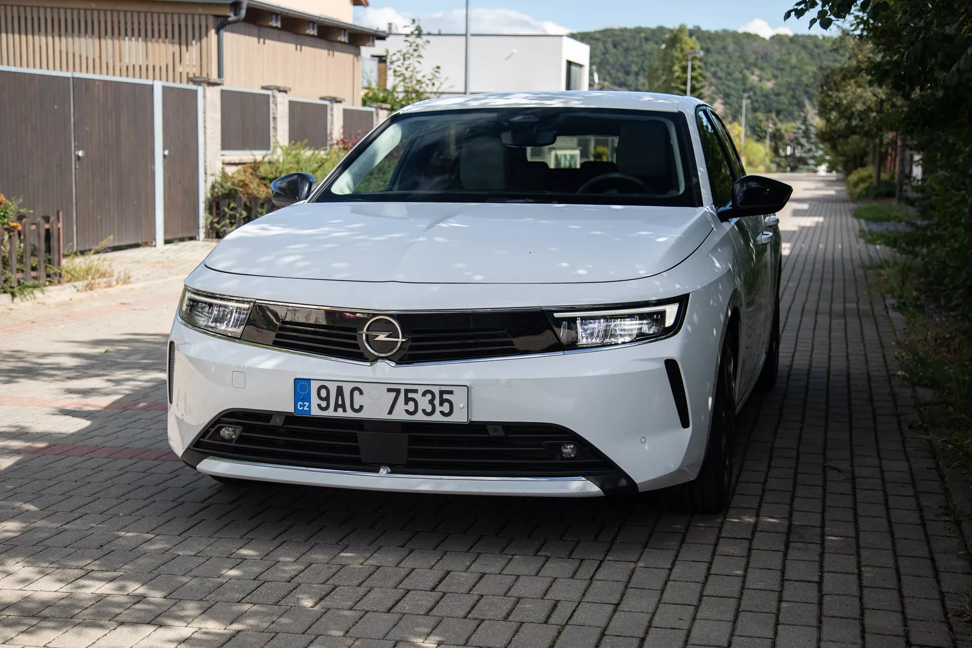 Vista frontale e laterale di Opel Astra 2022 evidenziando fari LED, design della griglia minimalista, cerchi in lega parzialmente visibili e pannelli della carrozzeria eleganti su una strada residenziale europea
