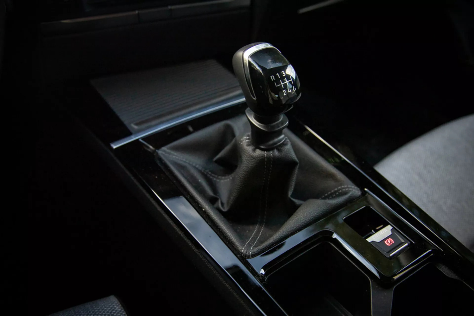 Primo piano del cambio manuale dell'Opel Astra 2022 nel quadrante superiore destro con copertura in pelle, console nera lucida e elementi interni circostanti