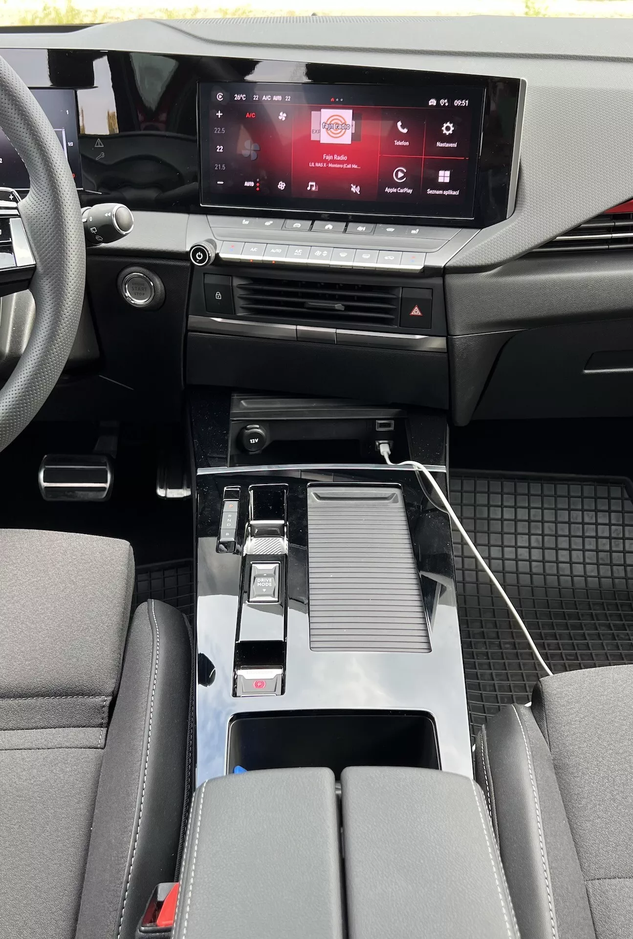 Vista interna dell'Opel Astra 2022 che mostra design moderno della cabina con sistema di infotainment touch-screen, controlli clima touch-sensitive, leva del cambio metallica, connettività USB, portabicchieri, bracciolo centrale dettagliato, sedili bicolore e dettagli della cabina in materiali misti con tappetini duraturi