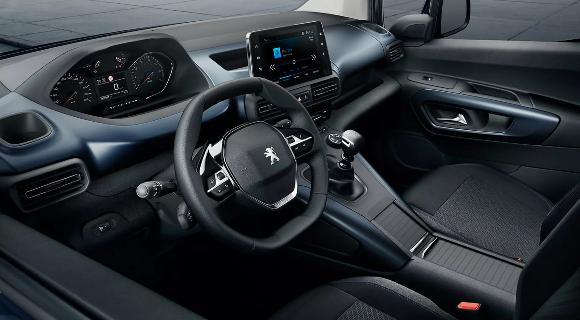 Visuale rialzata dell'interno del Peugeot Rifter 2018 con sistema di infotainment touchscreen, cruscotto digitale, e volante a tre razze con comandi integrati, evidenziando eccellenza tecnologica e di design
