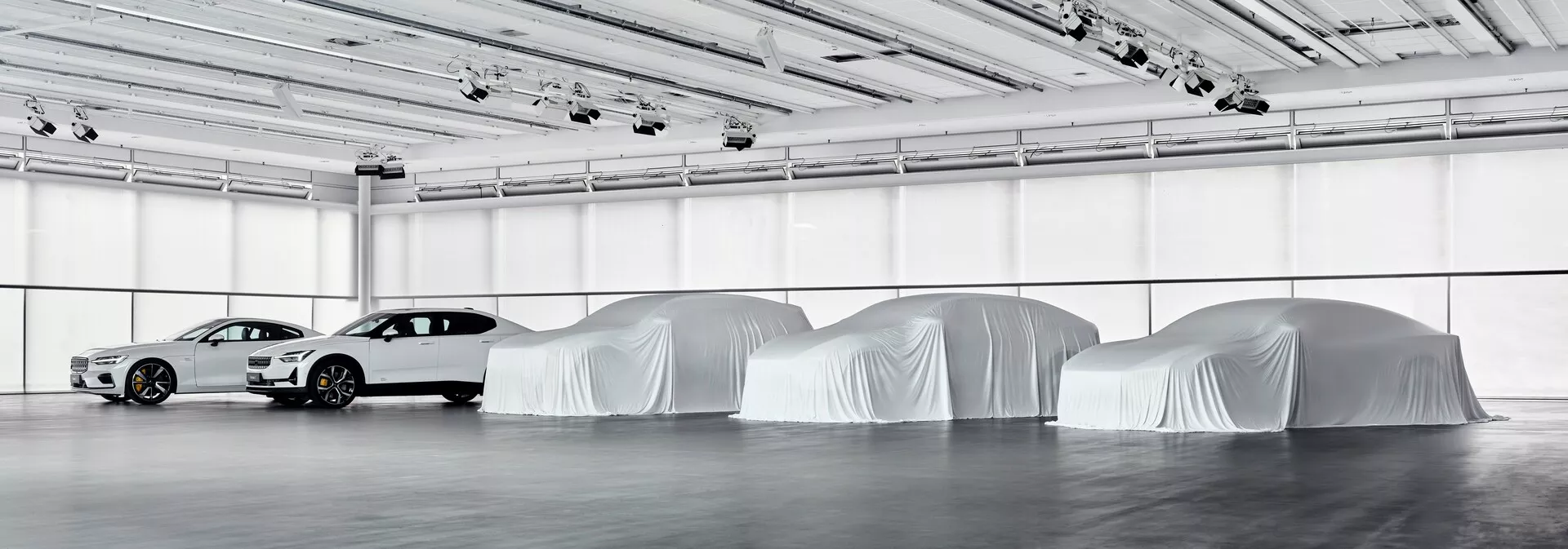 Debutto del Polestar 3 2023 che mostra il profilo di una berlina moderna con design aerodinamico in un ambiente espositivo interno, circondato dalla silhouette di futuri modelli sotto copertura