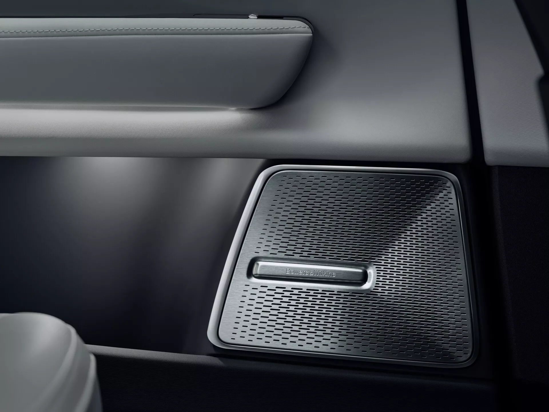 Dettaglio interno di un Polestar 3 2023 che mostra la griglia dell'altoparlante di alta gamma sul pannello della porta dell'auto, caratterizzata da un motivo a maglia densa per un suono ad alta fedeltà, design bicolore in similpelle con cuciture e una finitura metallica illuminata dolcemente che riflette la qualità del sistema audio del veicolo.