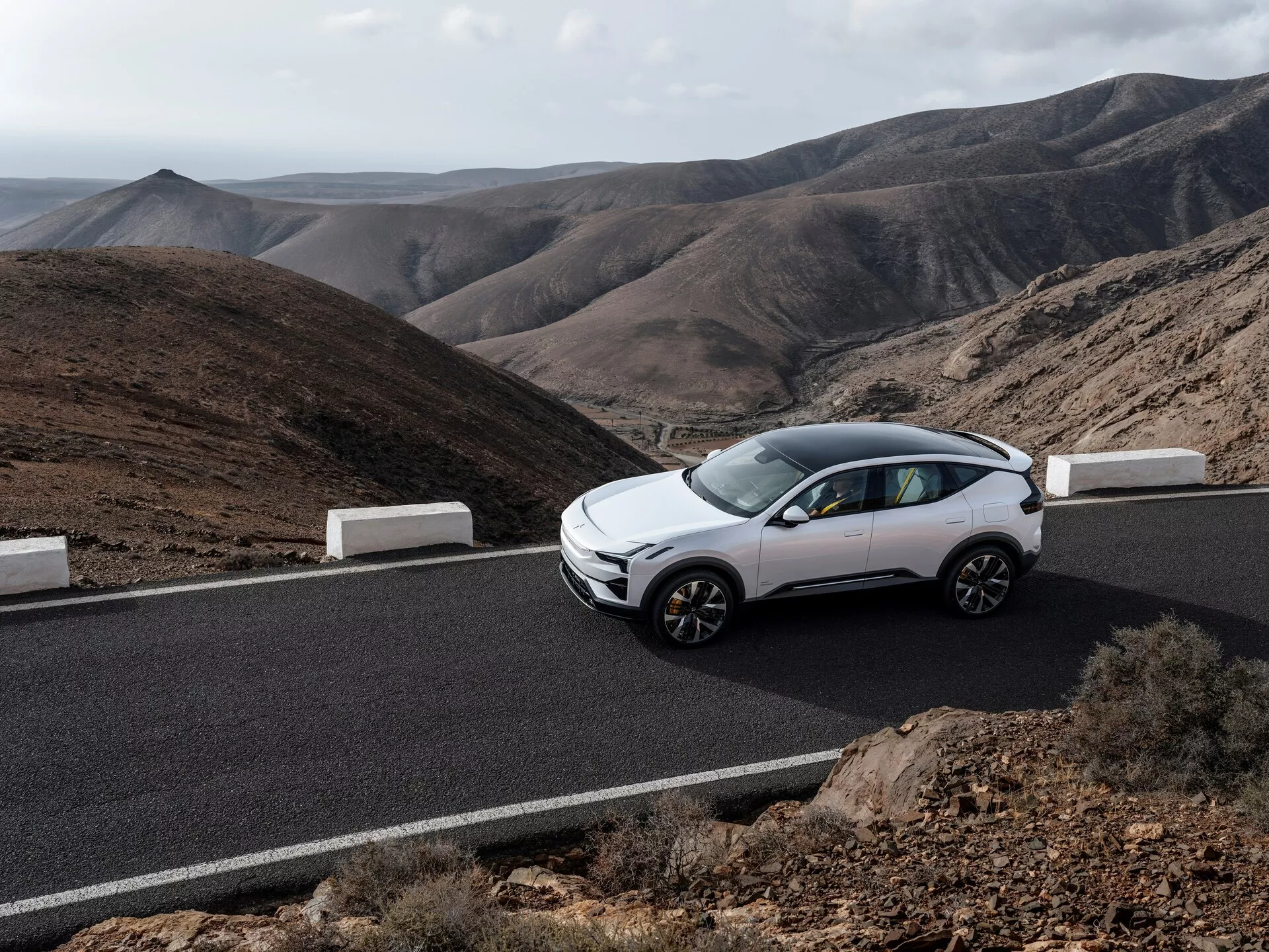 Polestar 3 prima generazione 2023, colore bianco, visto da un angolo frontale laterale su una strada d'asfalto con montagne sullo sfondo, evidenziando il suo design da crossover moderno, caratteristiche da SUV compatto e cerchi in lega sotto luce naturale.