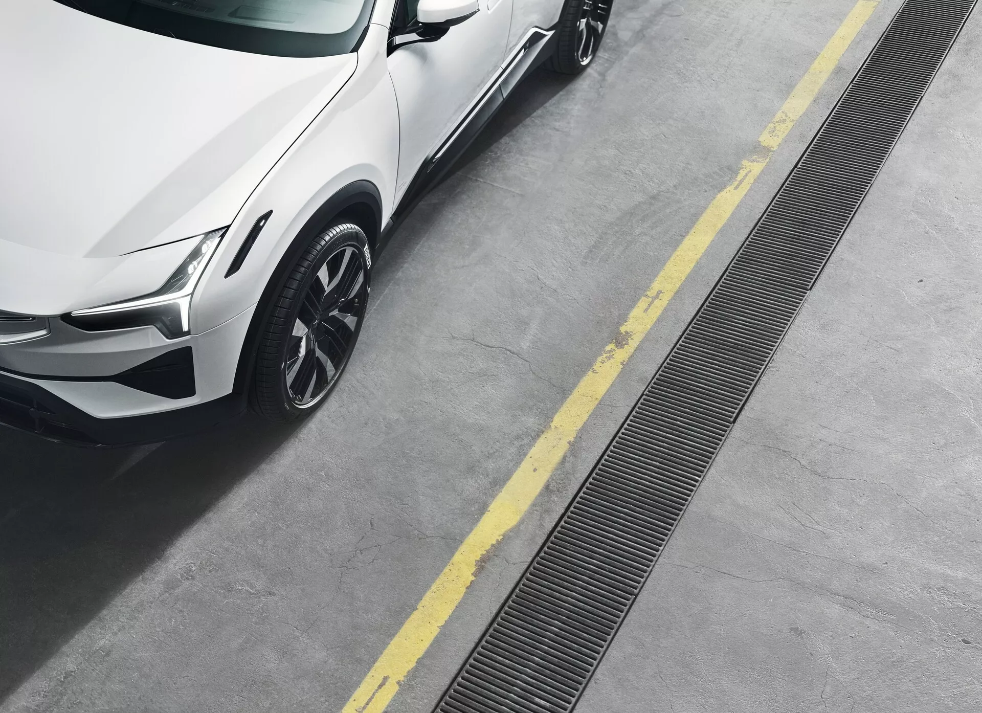 Polestar 3, 2023, prima generazione, vista da un angolo elevato che mostra il quarto anteriore destro, incluse la faro a LED, vernice metallizzata, ruota in lega a più razze e le linee dinamiche della carrozzeria su una superficie di cemento pulita con linee gialle di parcheggio.