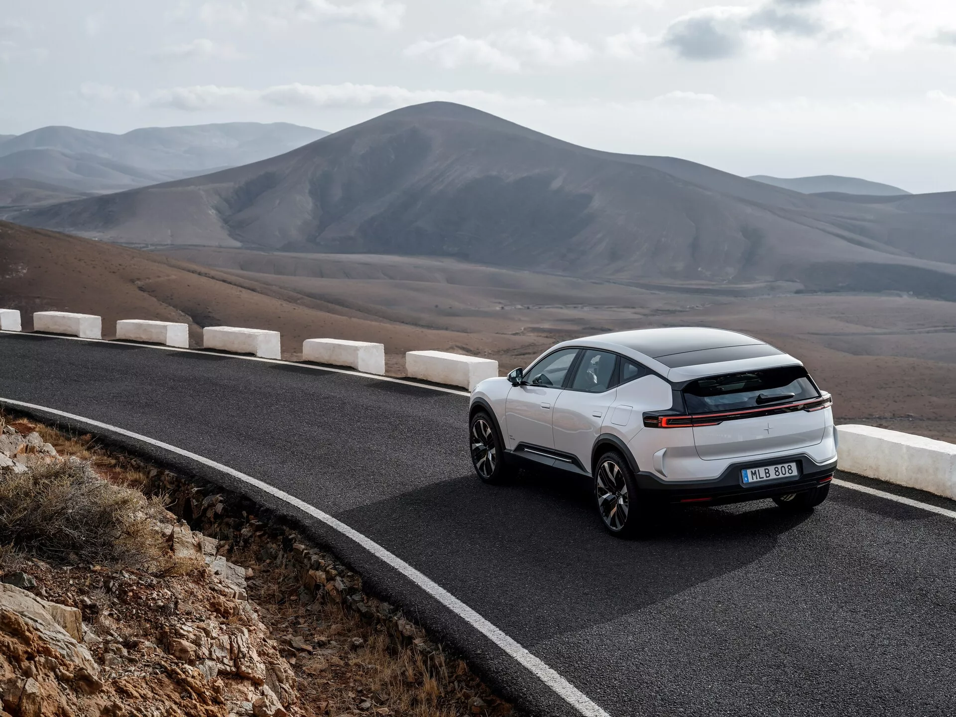 Polestar 3 1a generazione 2023 esposta in una vista dinamica da tre quarti posteriore su una strada di montagna tortuosa, evidenziando il suo esterno aerodinamico, moderna striscia di luci LED e design sportivo tipo coupé contro uno sfondo montano scenico, sottolineando la guida ecologica senza scarico visibile, suggerendo tecnologia elettrica o ibrida.