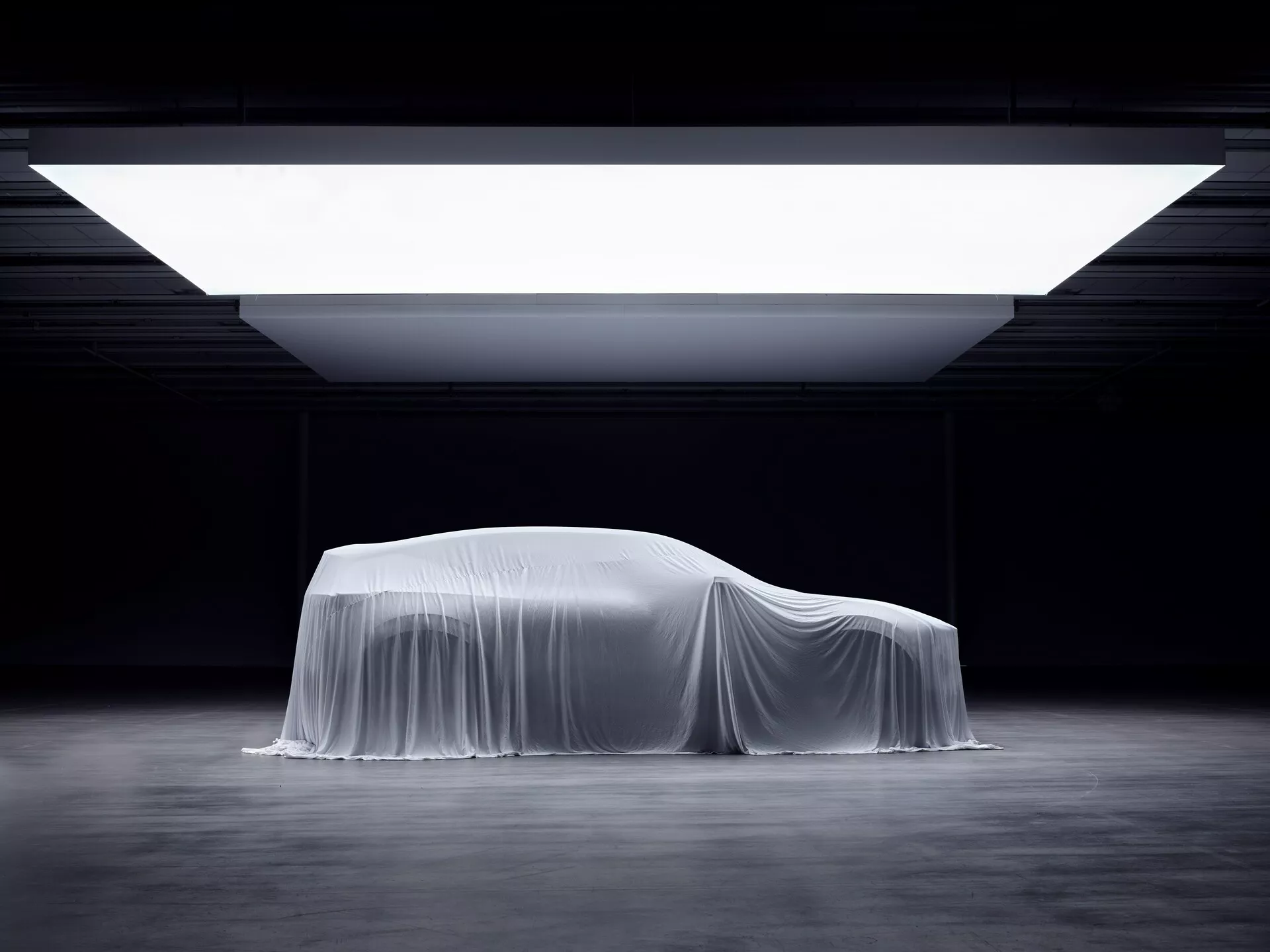 Rivelazione del Polestar 3 prima generazione 2023 sotto telo con profilo laterale che enfatizza il design aerodinamico e i contorni coupé, sotto un'illuminazione spettacolare da showroom