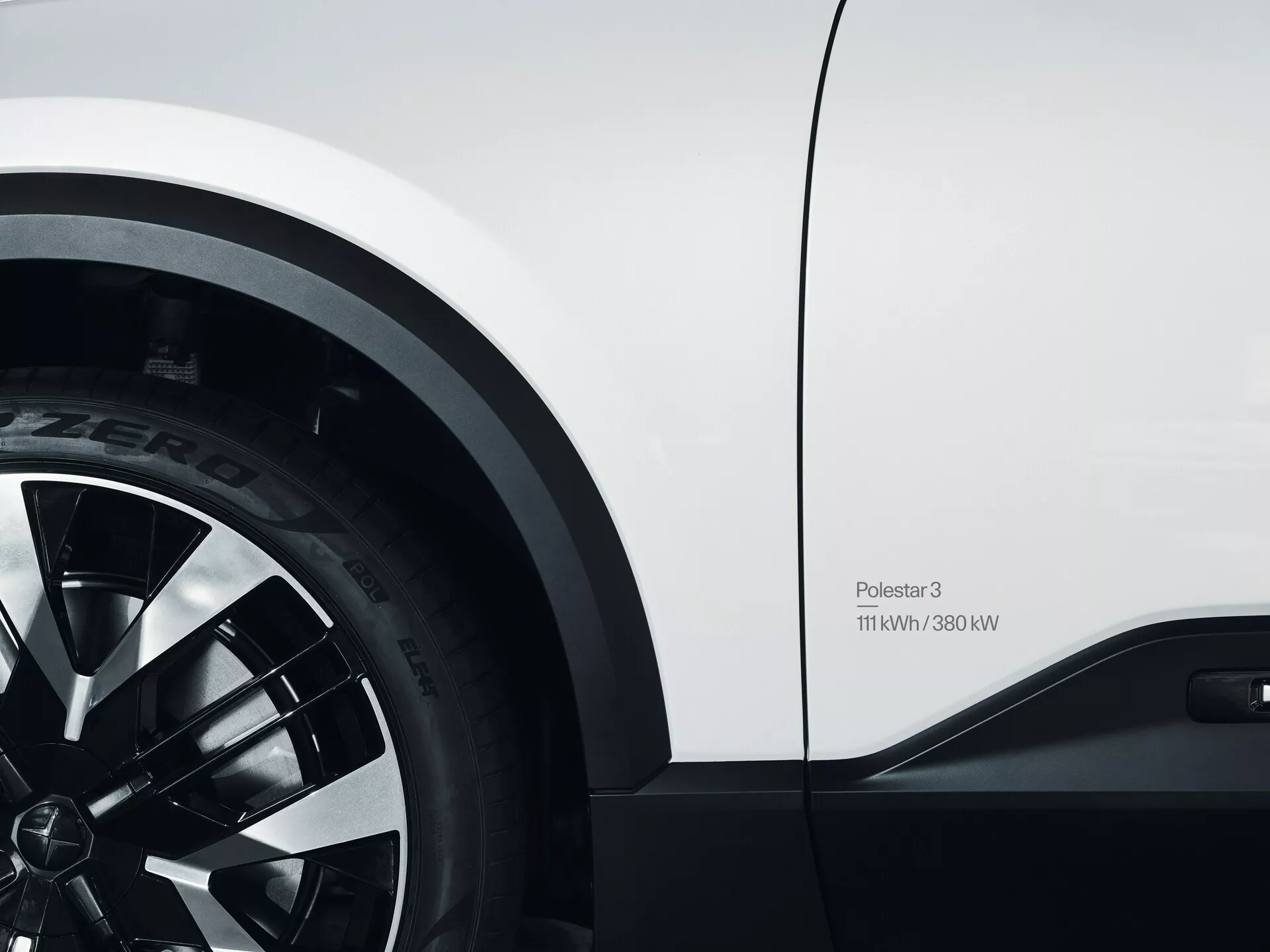 Vista ravvicinata del Polestar 3 2023 che mostra la ruota anteriore con pneumatico Pirelli P Zero e il pannello laterale, con design a razze multiple in lega e badge di specifiche di potenza 11kW/380kW, evidenziando le sue capacità di performance elettriche e il design elegante bianco.