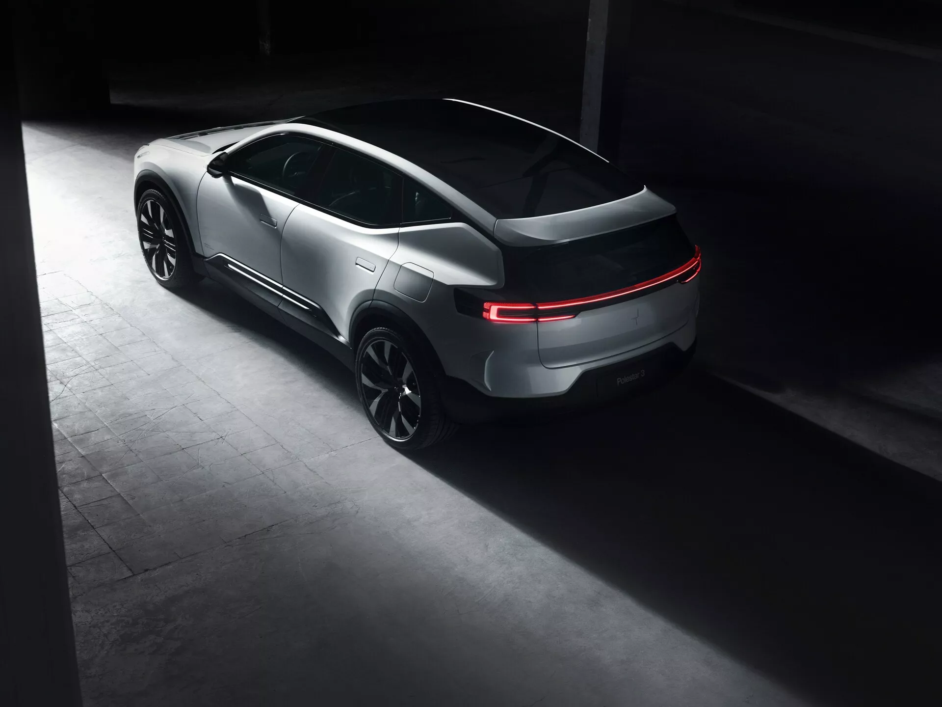 Polestar 3 prima generazione 2023, mostra un design elegante simile a un coupé con luci posteriori LED illuminate e grandi cerchi in lega sportivi in un ambiente poco illuminato di alta gamma, che sottolinea il suo fascino lussuoso e moderno