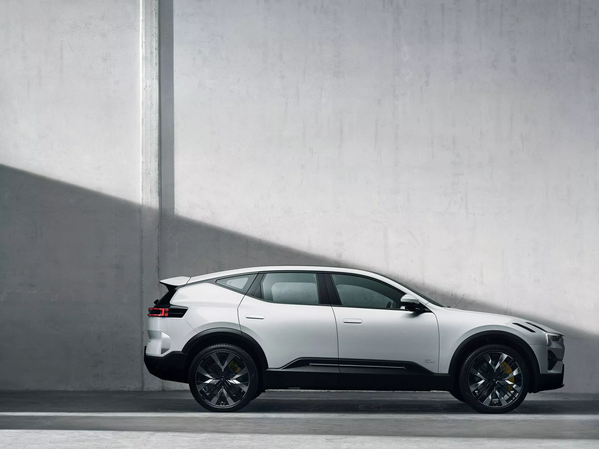 Vista laterale del SUV Polestar 3 del 2023 su sfondo grigio chiaro che evidenzia la sua silhouette sportiva da coupé, design a cinque porte, ruote intricate a più razze e linee caratteristiche che suggeriscono movimento, in condizioni di luce naturale che suggeriscono una vernice opaca e una sensazione moderna e lussuosa.