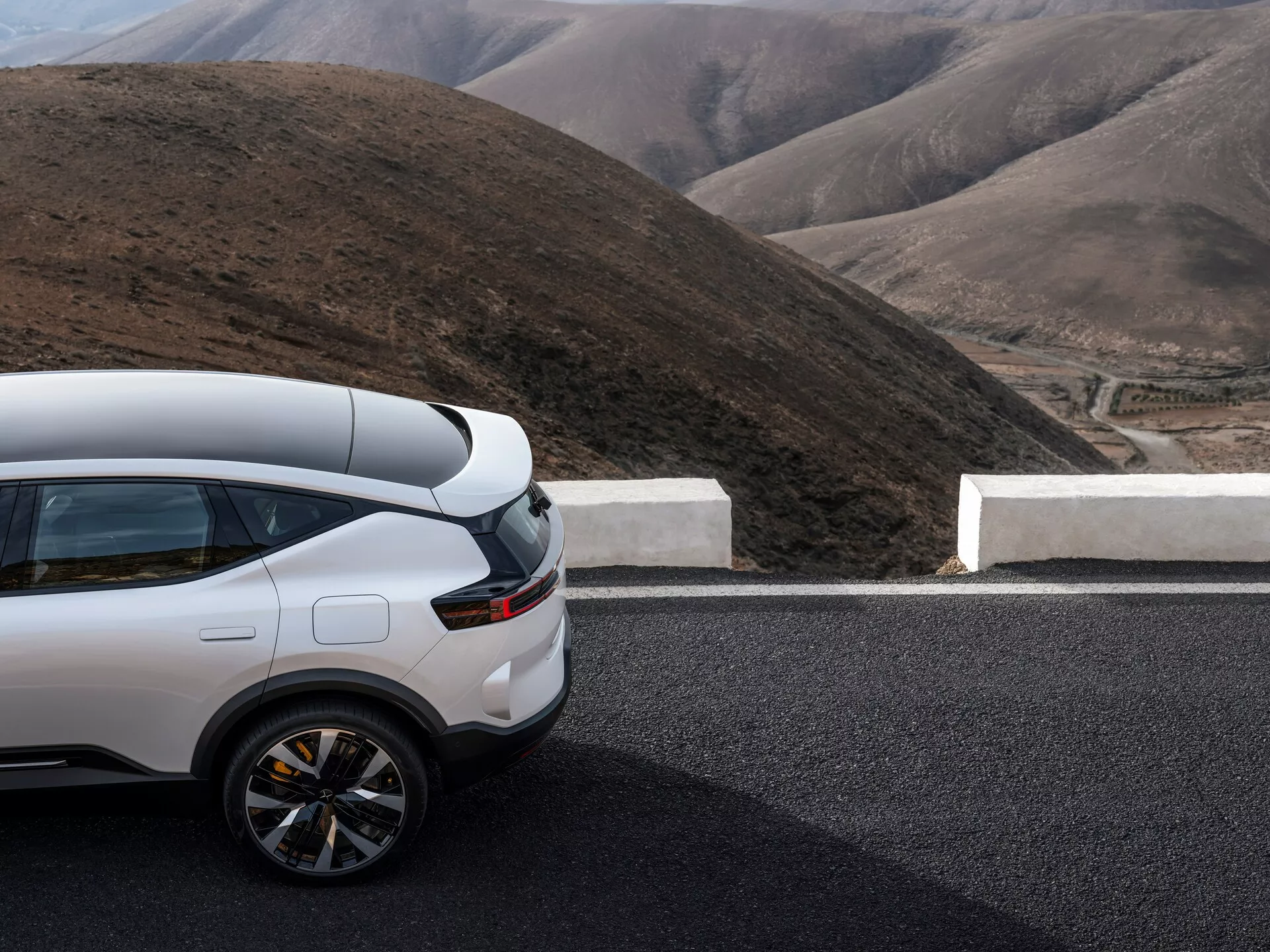 Polestar 3 prima generazione 2023 con vista parziale laterale e posteriore su una strada, con un SUV bianco high-tech su uno sfondo montuoso che enfatizza la sua parte posteriore sportiva, design dei fanali posteriori contemporaneo e profilo laterale lussuoso