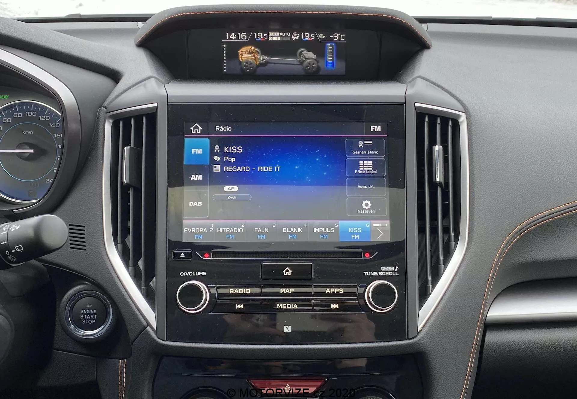 Vista ravvicinata dell'interno della Subaru XV 2018 (Subaru-XV-1-6i-Trend-Lineartronic) con focus sul sistema di infotainment centrale. Il display touchscreen, di circa 8-10 pollici, mostra un'interfaccia radio con FM selezionata. Gli elementi circostanti includono pulsanti fisici e manopole per il controllo manuale, un display più piccolo sopra che indica -3°C, 14:16 e 19/05, e le bocchette d'aria simmetriche. Il materiale intorno al sistema ha una finitura nera o grigio scuro metallica, tipica degli interni delle auto moderne. È visibile anche una parte del cruscotto e del volante.
