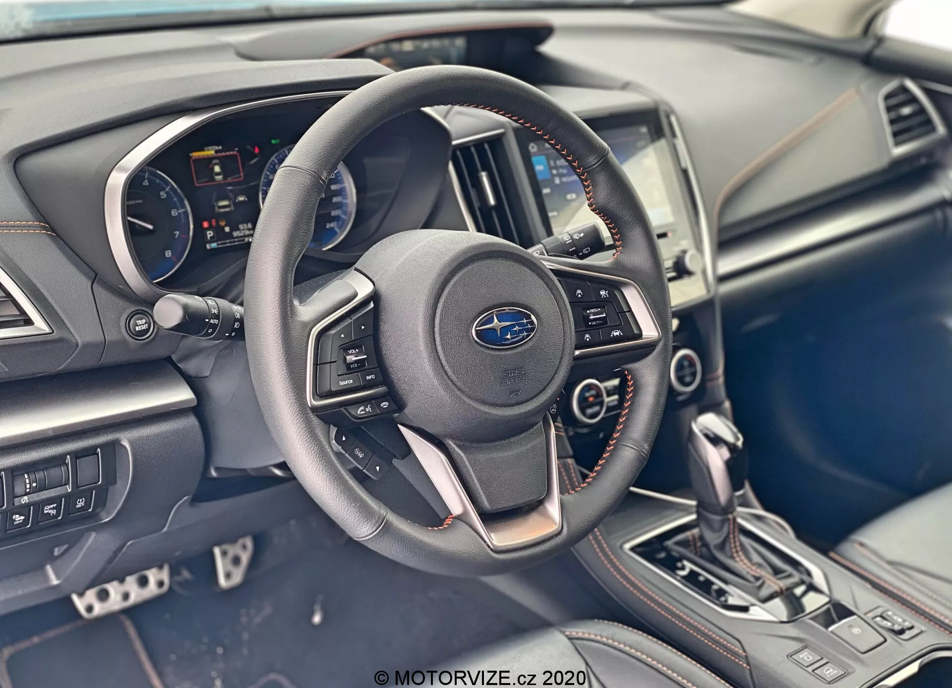 Vista dettagliata degli interni della Subaru XV 2018 (Subaru-XV-1-6i-Trend-Lineartronic) focalizzata sull'area del conducente, che mostra un cruscotto funzionale con un volante marcato Subaru con comandi integrati per audio e chiamate in vivavoce, un quadro strumenti visibile con tachimetro, contagiri e display digitale, un display infotainment centrale integrato nel cruscotto, nonché pulsanti di controllo del clima. La console centrale ha una leva del cambio automatica in posizione di parcheggio e altri pulsanti per le modalità di guida, insieme a materiali moderni e dettagli di design eleganti.