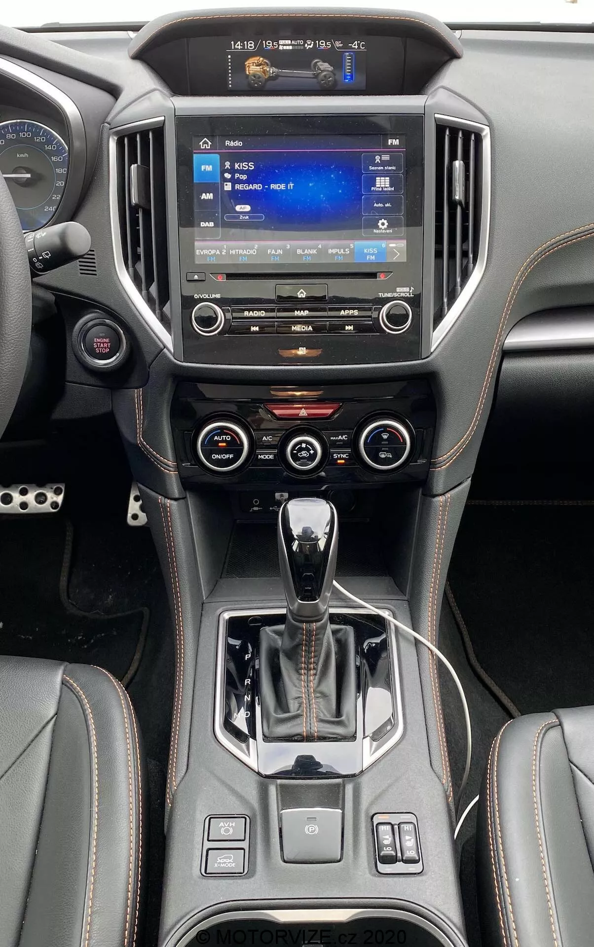 Vista della console centrale e del cruscotto della Subaru XV 2018 dal sedile posteriore, con un ampio touchscreen per l'infotainment con navigazione, pulsanti fisici per il controllo del clima, leva del cambio automatico, freno di stazionamento elettronico, rivestimenti in pelle premium con cuciture a contrasto.
