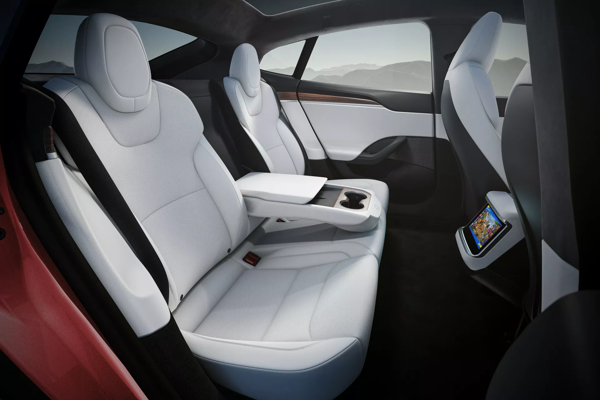 Interno della Tesla Model S 2016 (facelift di 1ª generazione) che mostra sedili di lusso in pelle bianca con accenti neri, design ergonomico e ampio spazio per le gambe. L'immagine cattura i sedili sul lato destro da una prospettiva angolata e leggermente sopraelevata, evidenziando la console centrale funzionale che termina prima dei sedili posteriori, con un touchscreen per i passeggeri posteriori e ricarica wireless per smartphone. Tettuccio panoramico in vetro che offre luce naturale e una sensazione di apertura.