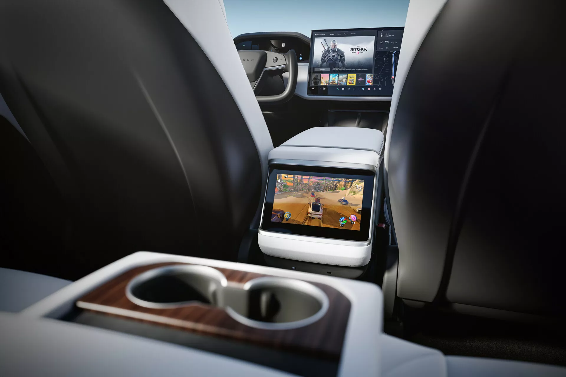 Vista interna della Tesla Model S 2016 (prima generazione facelift) focalizzata sul comparto passeggeri posteriori. Prospettiva dal sedile posteriore all'altezza del cuscino mostrando due sedili anteriori con poggiatesta, console centrale e schermo incorporato sul retro del sedile anteriore del passeggero. Tecnologie di intrattenimento per i passeggeri posteriori evidenti con schermo attivo che mostra contenuti multimediali. Caratteristiche includono bracciolo pieghevole con portabicchieri integrati e finitura in legno, visione parziale del cruscotto anteriore con schermo più grande per infotainment e materiali di lusso. Interni ben illuminati con toni neutri che indicano un veicolo di lusso contemporaneo.