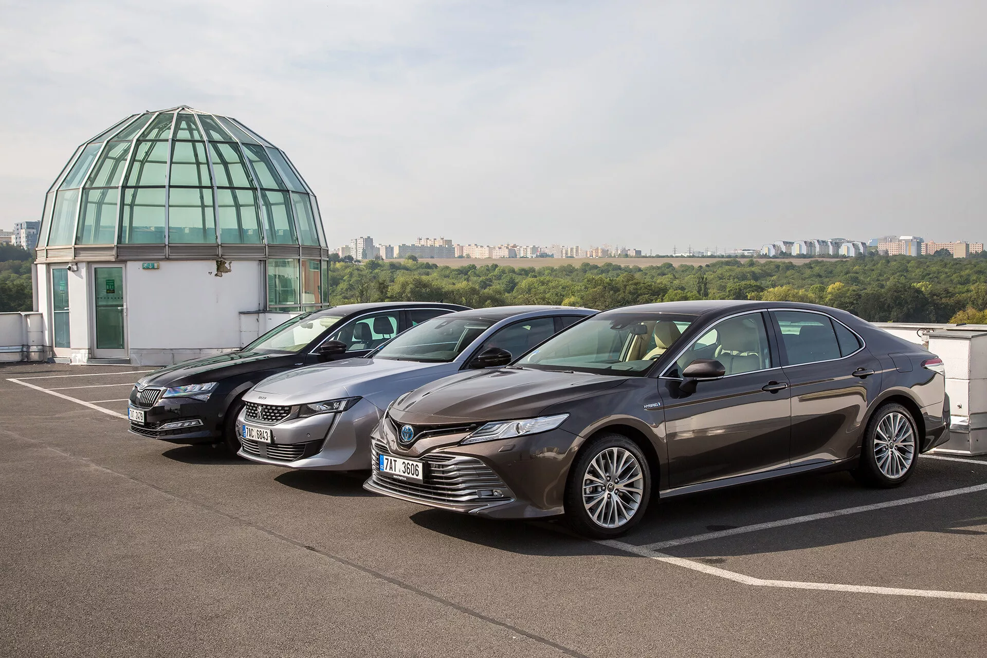 Limousine Toyota Camry 2019 parcheggiata su un terrazzo all'aperto con cielo sereno e cupola di vetro sullo sfondo, che mostra un design moderno con griglia frontale dinamica, fari LED affilati, cofano scolpito e cerchi in lega di lusso