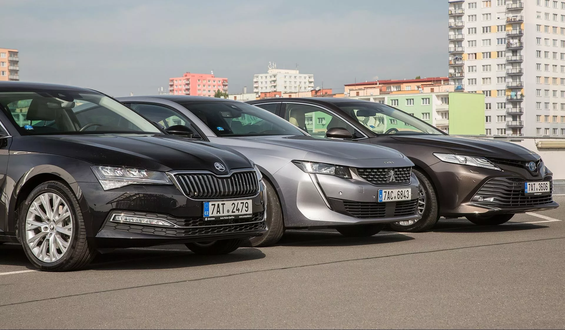 Linea di Toyota Camry 2019, con modelli in colori scuro, argento e grigio in ambiente urbano, presentando vista frontale tre quarti con fari LED ed elementi di design eleganti