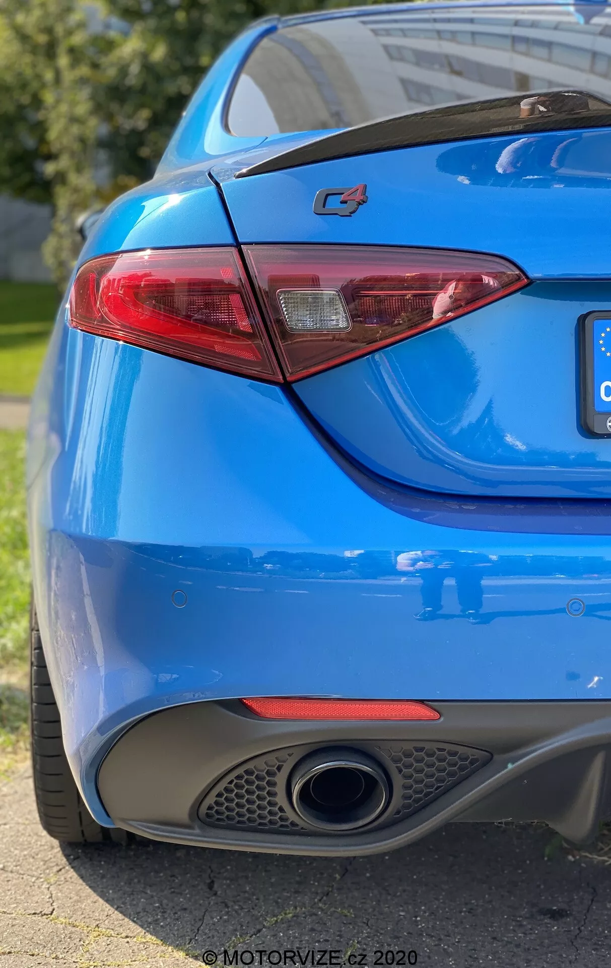 Primo piano della sezione posteriore di un'auto blu mostrante il lato destro da un angolo basso di tre quarti. L'inquadratura cattura il prominente emblema 'C4' sul bagagliaio, un’elegante luce posteriore a LED, la vernice blu vivace, uno scarico cromato singolo e il diffusore integrato nel paraurti posteriore. La scarsa profondità di campo mette in risalto l'emblema e la luce posteriore, mentre la luce solare naturale si riflette sulle curve lisce e sportive della carrozzeria.