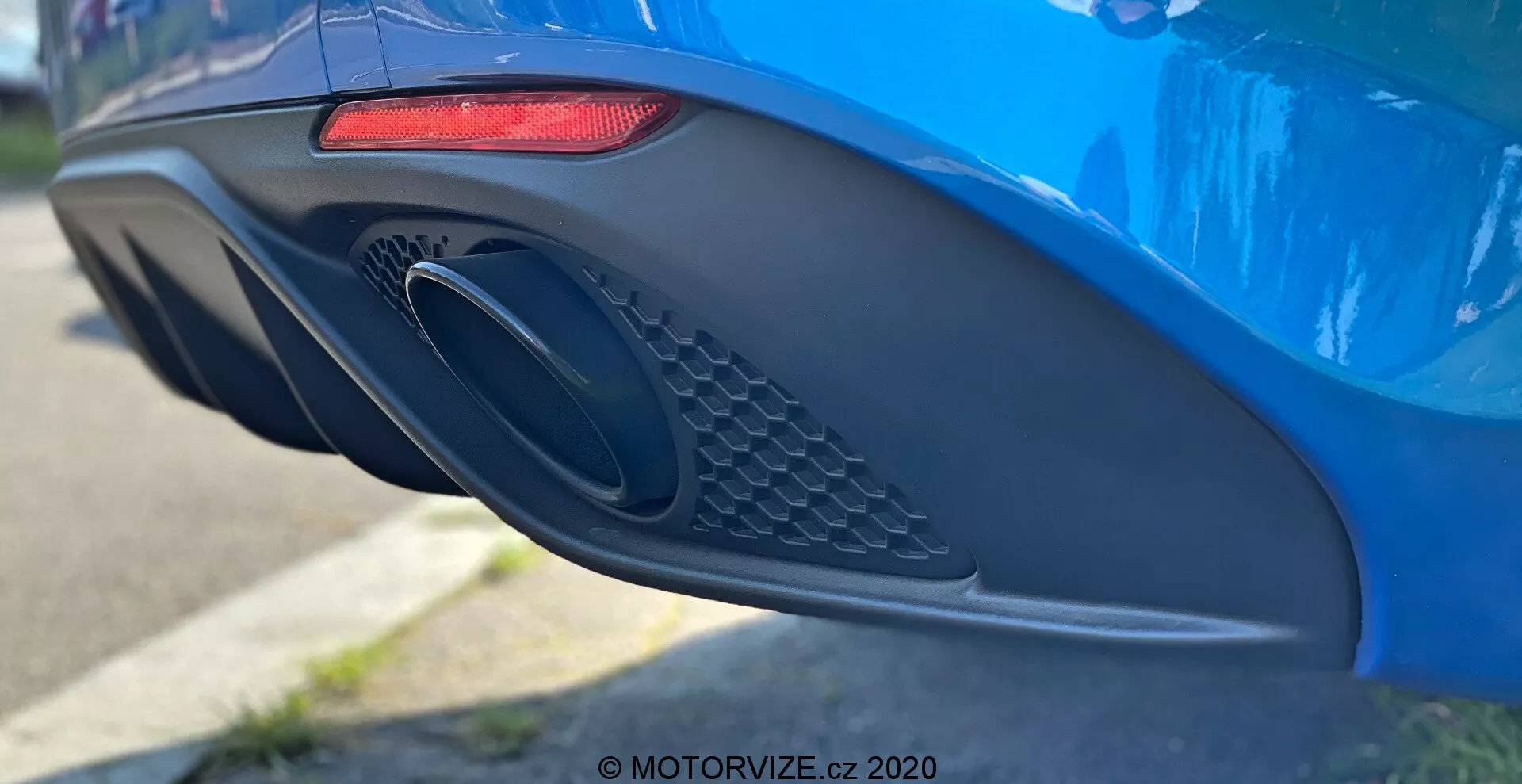 Primo piano del lato posteriore di un Alfa Romeo Giulia 2016 blu vibrante che mette in evidenza le caratteristiche di design moderne, inclusi un fanale posteriore a LED rosso orizzontale allungato, un grande scarico ovale con dettaglio a rete e un paraurti aerodinamico con varie curve e rientranze, fotografato con una ridotta profondità di campo per enfatizzare i dettagli dell'auto.