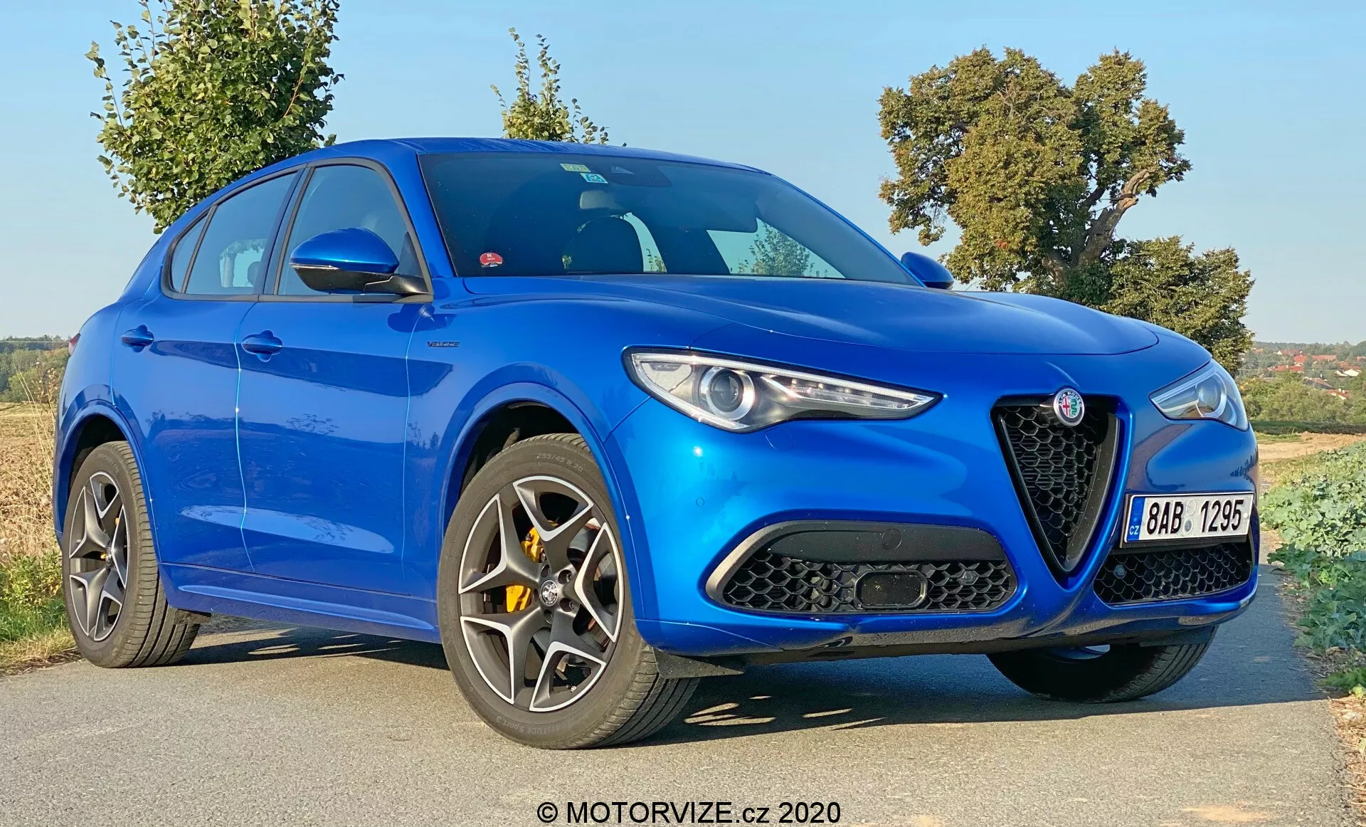 Vista a tre quarti anteriore dell'Alfa Romeo Stelvio 2017 in blu brillante, con una distintiva griglia triangolare con un logo prominente, eleganti fari stretti, contorni pronunciati del cofano e ruote a più raggi. Questa immagine cattura il design aggressivo e moderno del veicolo con grandi prese d'aria sul paraurti anteriore, una siluetta sportiva con una linea del tetto discendente e linee scolpite sul corpo, suggerendo un'identità orientata alle prestazioni e al lusso.