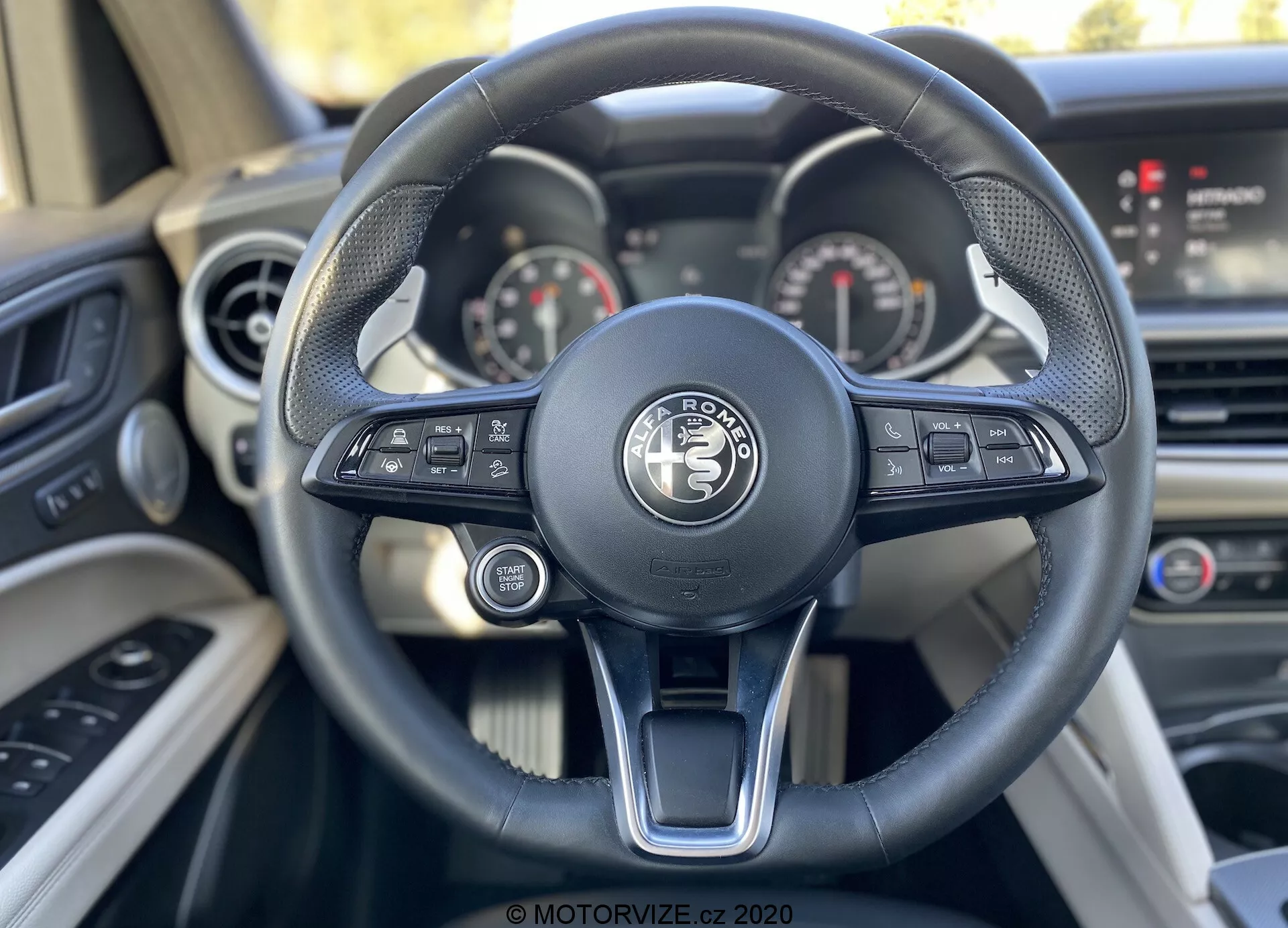 Vista ravvicinata della prospettiva del guidatore dal sedile del conducente in un veicolo Land Rover, che evidenzia il moderno volante a tre razze con comandi tecnologici integrati e il sofisticato cruscotto con quadranti analogici e uno schermo digitale.