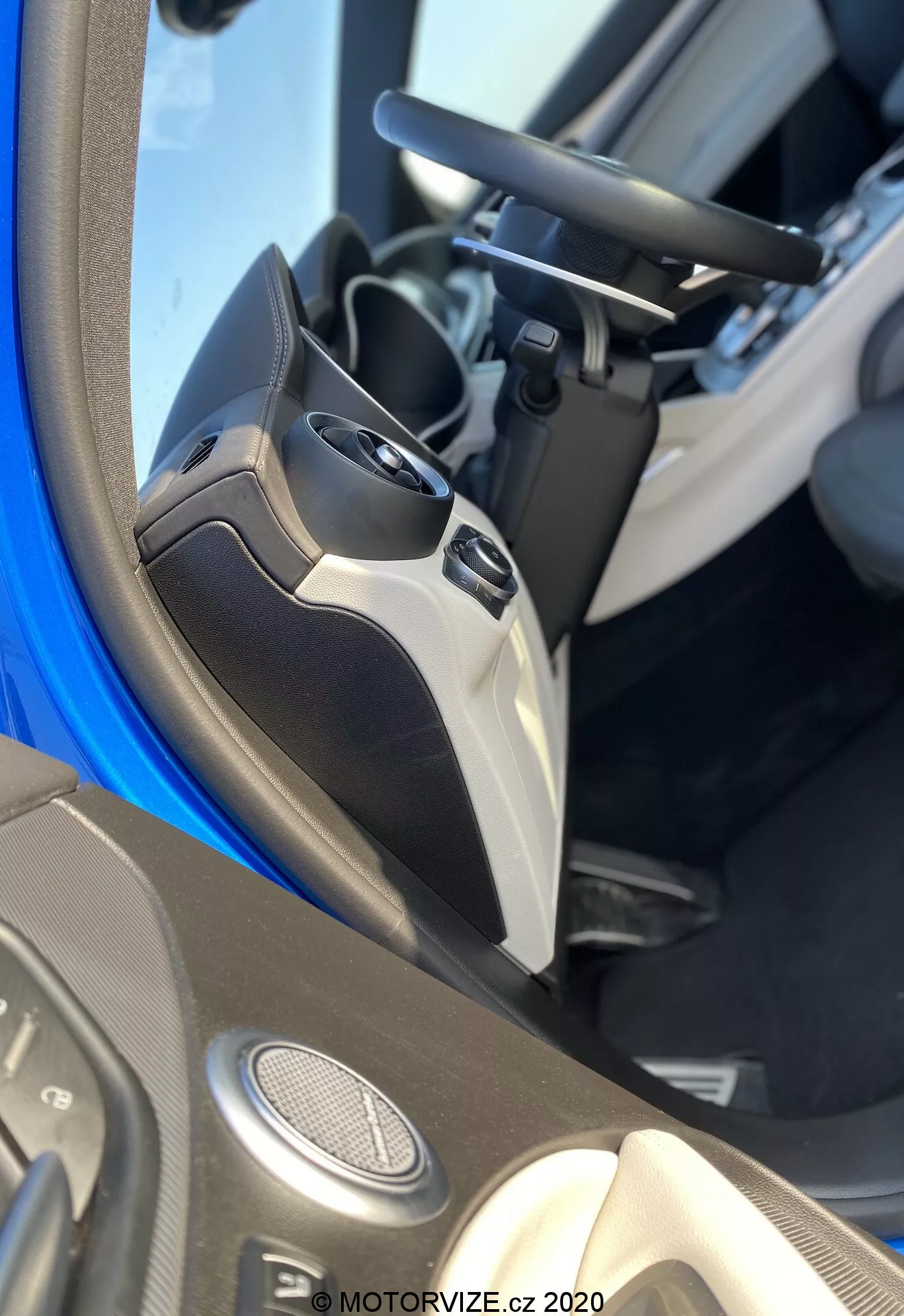Primo piano degli interni dell'Alfa Romeo Stelvio 2017 con un focus sul pannello della portiera del conducente. L'inquadratura cattura la metà inferiore della portiera e parte del sedile del conducente, mostrando varie caratteristiche tecnologiche. Il pannello include altoparlanti montati sulla portiera che suggeriscono un sistema audio avanzato, comandi a vetro elettrici con vari pulsanti per la funzionalità one-touch, e un controllo di regolazione dello specchietto laterale elettrico. È visibile anche la maniglia della portiera, integrata nel design. I materiali utilizzati implicano un particolare livello di rifinitura o un pacchetto interni specifico, con una tasca portaoggetti nella parte inferiore. L'immagine è contrassegnata con 'MOTORVIZE.cz 2020'.