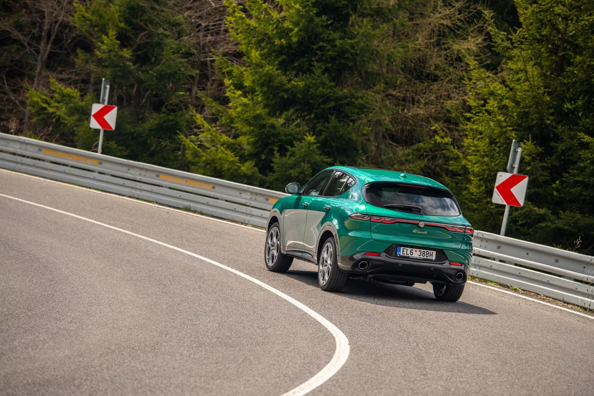 Alfa Romeo Tonale 2022 catturata da un angolo posteriore di tre quarti su una strada curva, evidenziando il suo design sportivo hatchback, finitura lucida e caratteristiche aerodinamiche tra cui uno spoiler posteriore, cerchi in lega e luci posteriori LED.