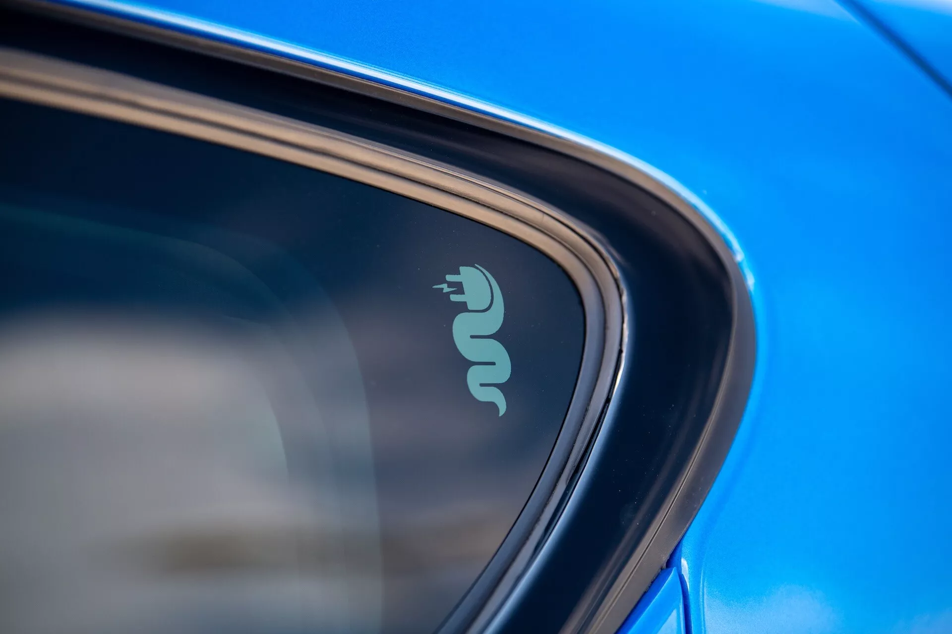 Primo piano dettagliato dell'Alfa Romeo Tonale 2022 che mostra il badge tecnologico indicativo della capacità elettrica o ibrida vicino al finestrino dell'auto, evidenziato da vernice blu riflettente e design elegante alla luce naturale del giorno
