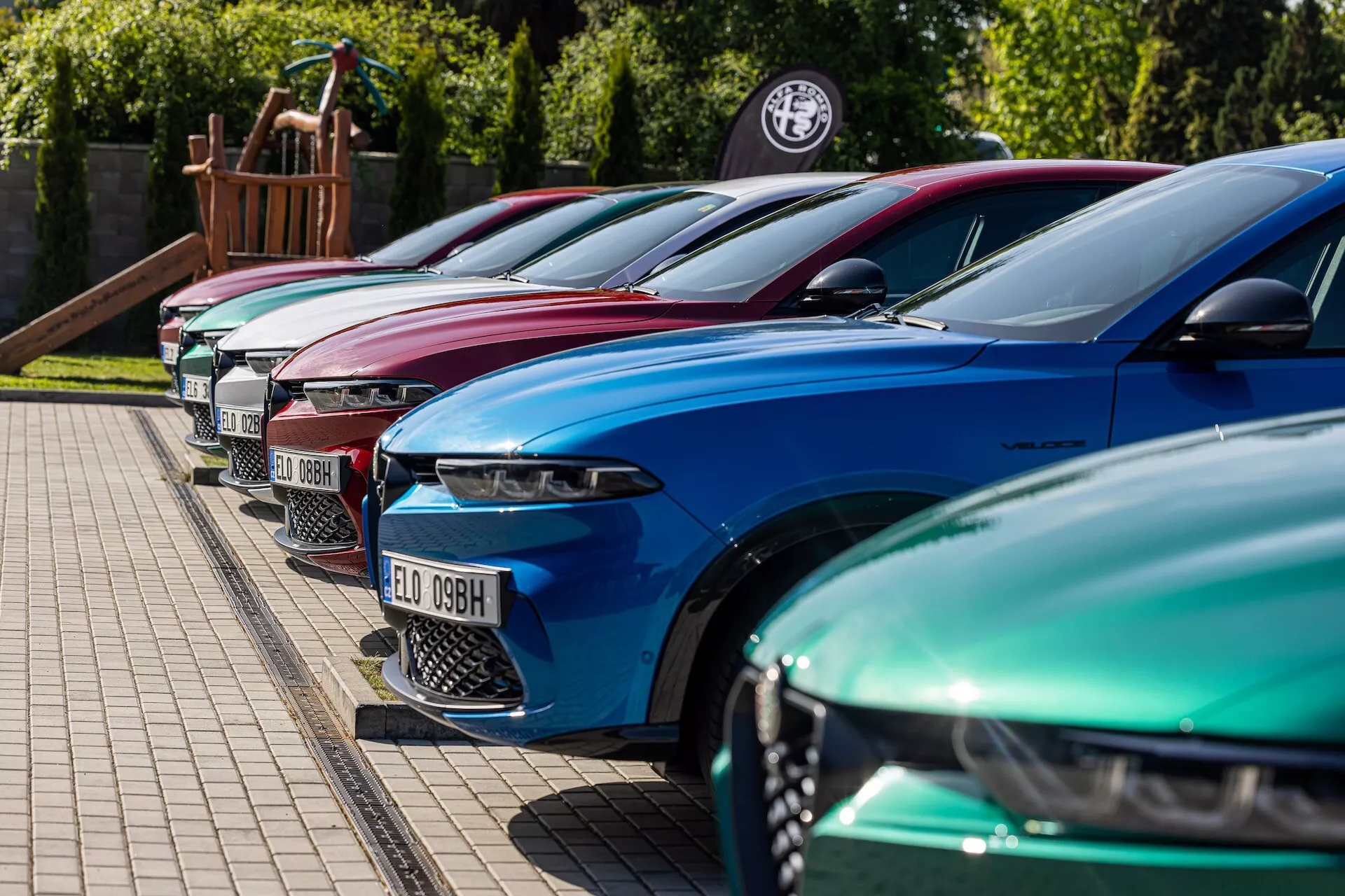 Linea di Alfa-Romeo Tonale 2022 in colori vivaci che mostra un design di lusso con fari LED avanzati, parcheggiata in formazione diagonale con una messa a fuoco sul lato anteriore sinistro da un angolo di altezza bassa a media su un'area pavimentata accanto a un bordo erboso, forse presso una concessionaria o un evento per appassionati di auto