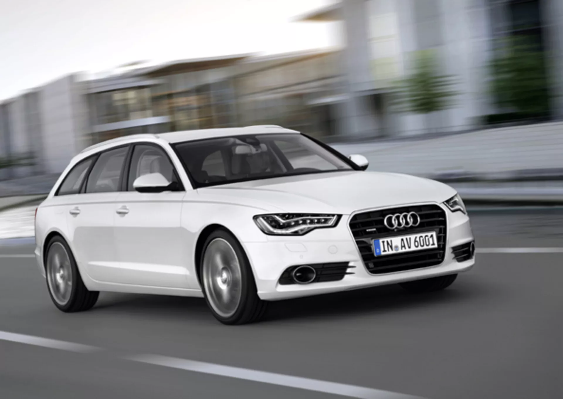 Audi A6 Avant bianca del 2011 in movimento, catturata da un angolo basso frontale tre quarti evidenziando la griglia, luci diurne a LED, cerchi in lega e design dinamico