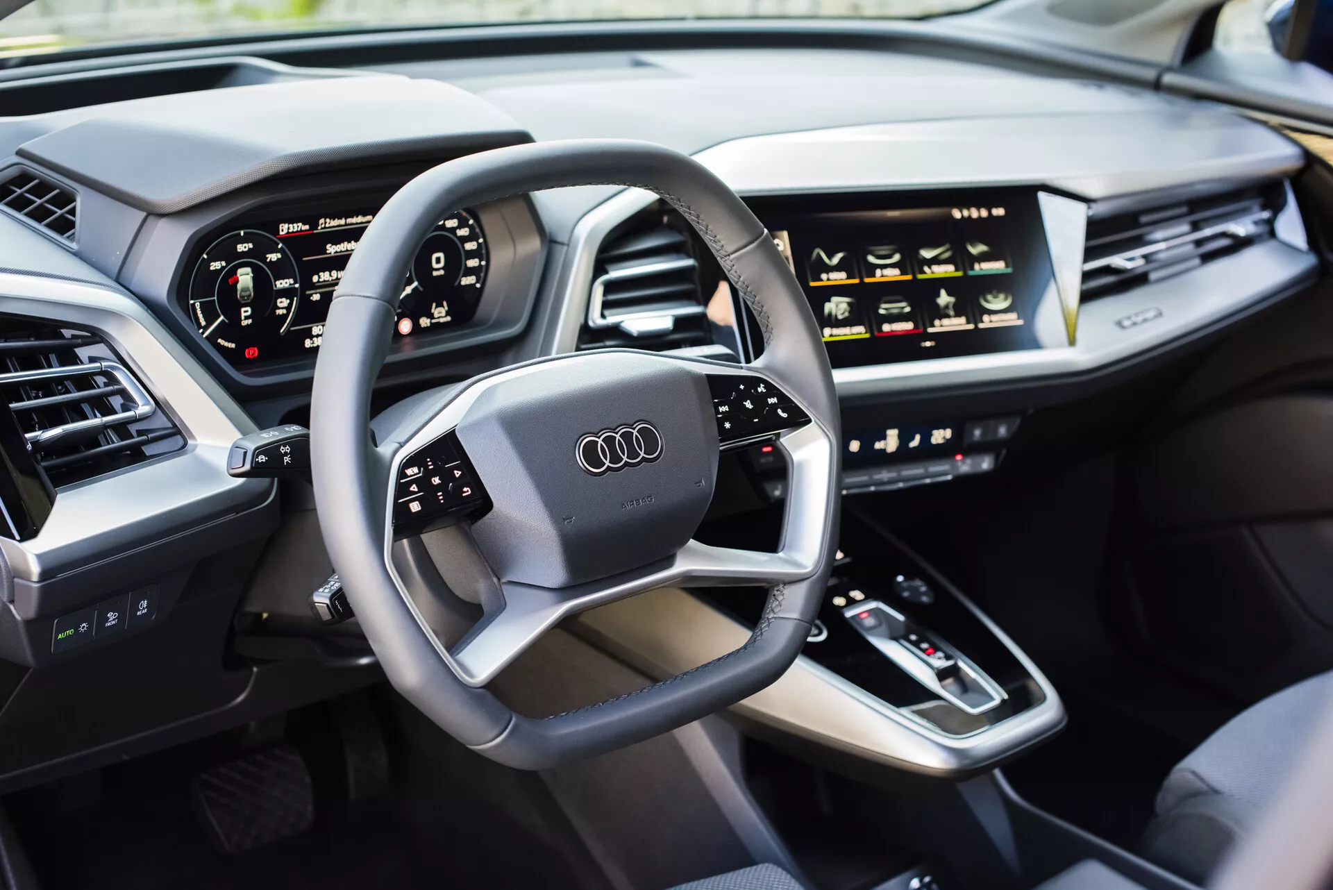 Vista interna di un Audi Q4 e-tron 2021 dal lato del conducente, con volante multifunzione con logo Audi, cruscotto digitale, console centrale con leva del cambio, comandi HVAC sensibili al tocco, display infotainment, cruscotto elegante con bocchette d'aria integrate e porta imbottita in pelle di lusso, mostrando la tecnologia automobilistica moderna e le caratteristiche dei veicoli di lusso.