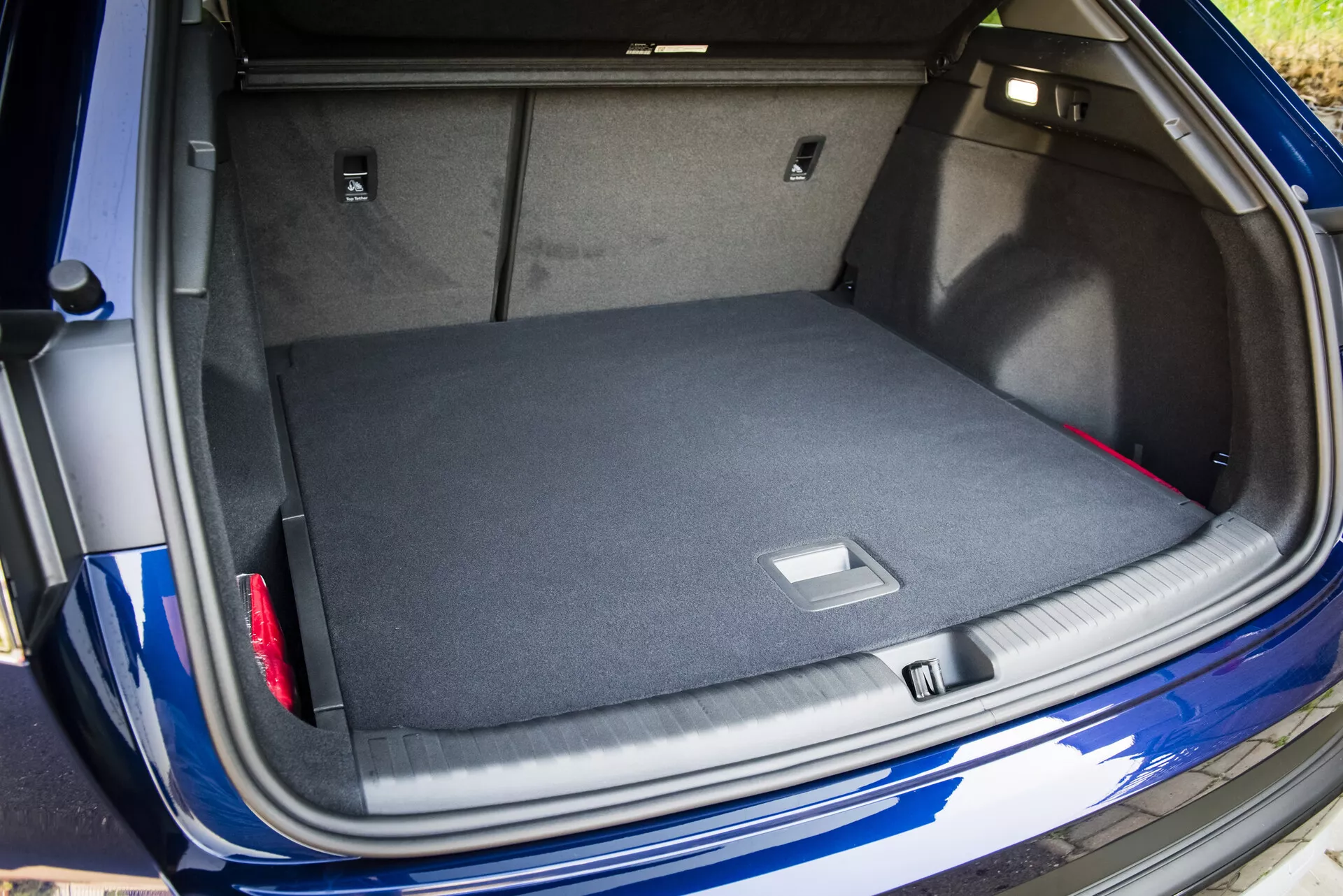 Vista dell'ampio bagagliaio moquette dell'Audi Q4 e-tron 2021 con il coperchio del bagagliaio aperto, che mostra soluzioni di stoccaggio intelligenti e un'occhiata al suo esterno blu metallico con sensore di parcheggio visibile