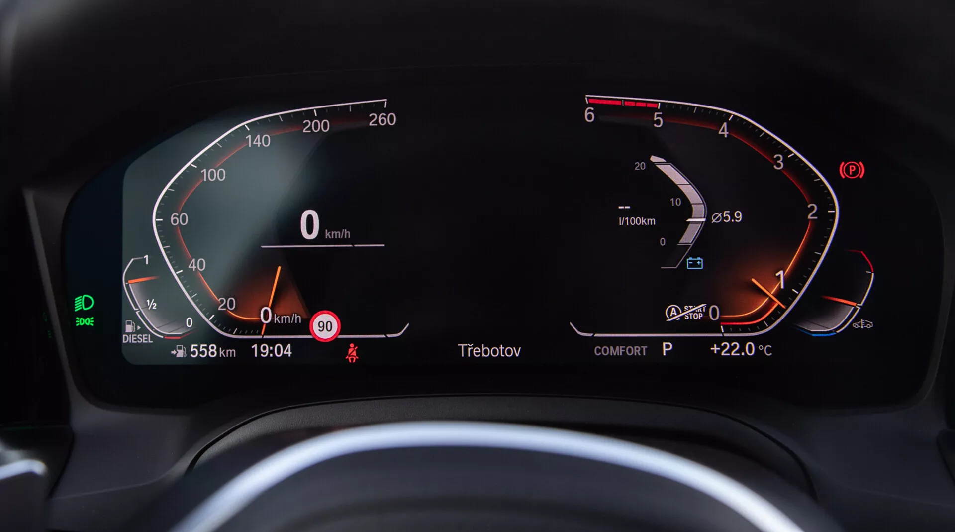 Immagine ravvicinata del quadro strumenti digitale della BMW 2 Series Coupe 2022, vista dal sedile del conducente. Il tachimetro digitale semicircolare a sinistra varia da 0 a 260 km/h, mostrando che il veicolo è fermo. Il contagiri a destra mostra il motore al minimo appena sopra 0 RPM. Integrato nel contagiri ci sono un indicatore di carburante digitale quasi pieno e un indicatore di temperatura del motore che indica il range normale. Il display digitale centrale mostra il contachilometri a 558 km, velocità a 0 km/h, avviso di velocità a 90 km/h, ora attuale 19:04, indicatore cambio 'P' per Park e temperatura esterna +22,0 °C. Si vede anche un'icona verde del sistema di assistenza alla corsia, la visualizzazione della modalità 'COMFORT', l'indicatore del carburante diesel e il promemoria delle cinture di sicurezza.