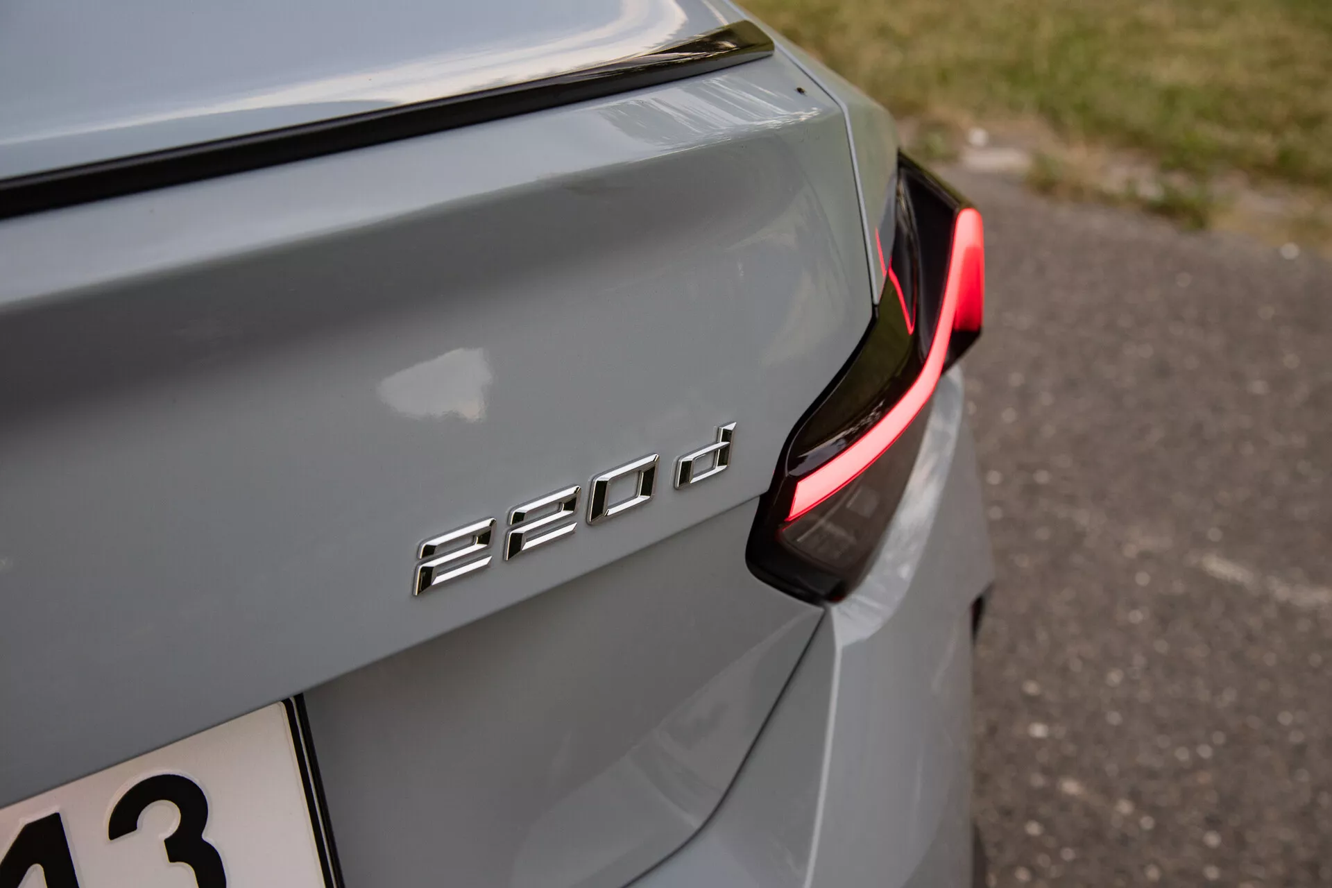 Dettaglio ravvicinato della sezione posteriore destra di una BMW 530d, evidenziando la designazione del modello '530d' e concentrandosi sul moderno fanale posteriore LED parzialmente illuminato. Il colore dell'auto è argento o grigio metallizzato con un riflesso morbido in luce naturale, che suggerisce un ambiente serale o ombreggiato. Il badge è cromato o metallico, in contrasto con la vernice dell'auto e posizionato sul cofano. Presenta una bassa profondità di campo che mette in evidenza il badge '530d' e la carrozzeria vicina mentre sfoca lo sfondo, adatto per appassionati di tecnologia automobilistica o design veicolare.