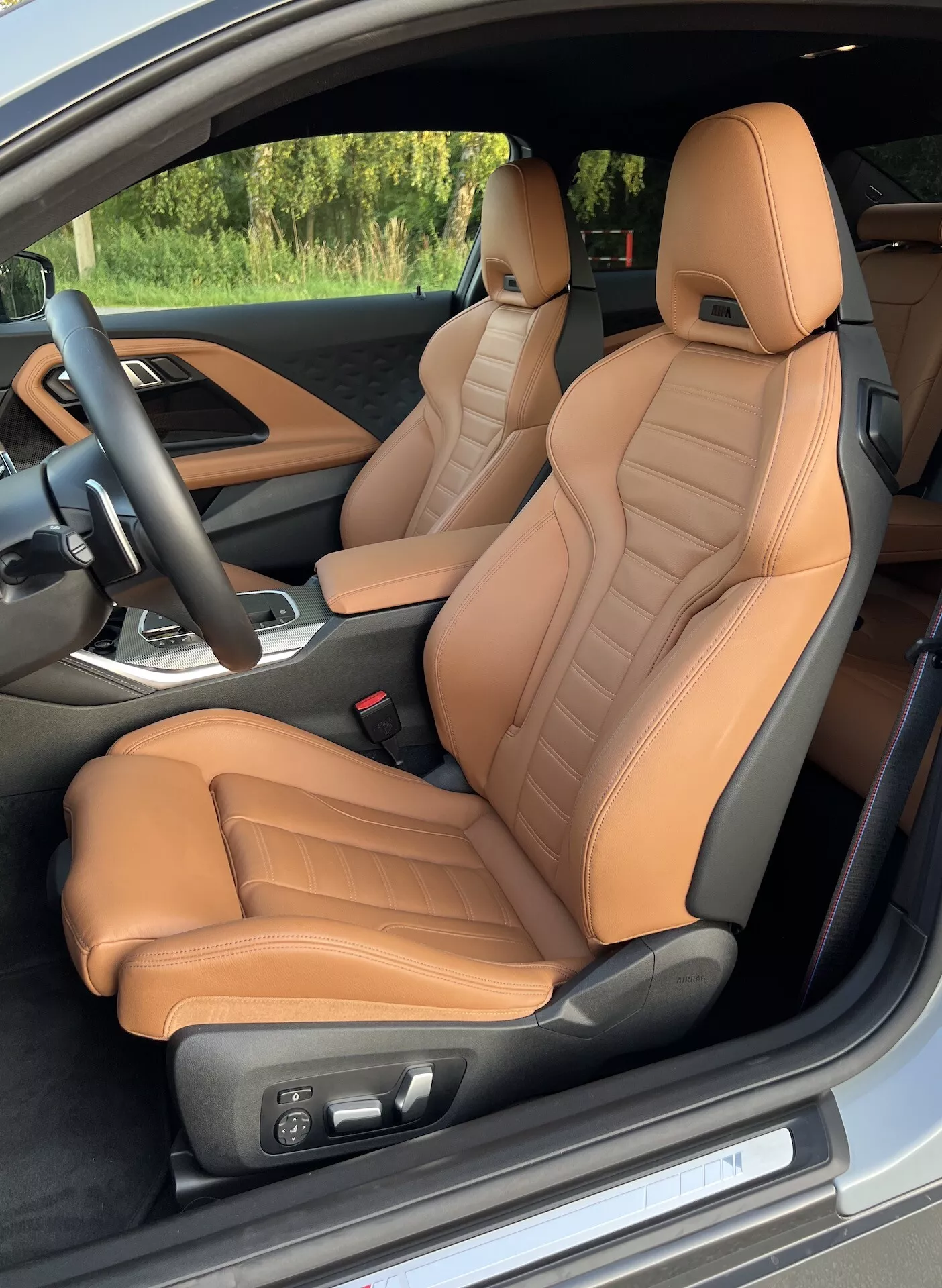 Vista interna della BMW Serie 2 Coupé 2022 dalla portiera lato guida, evidenziando i sedili anteriori rivestiti in pelle color cuoio con dettagli trapuntati e supporto ergonomico. Regolazioni elettriche dei sedili, un volante nero con comandi integrati e una vista parziale della console centrale con leva del cambio suggeriscono caratteristiche lussuose e orientate alle prestazioni.