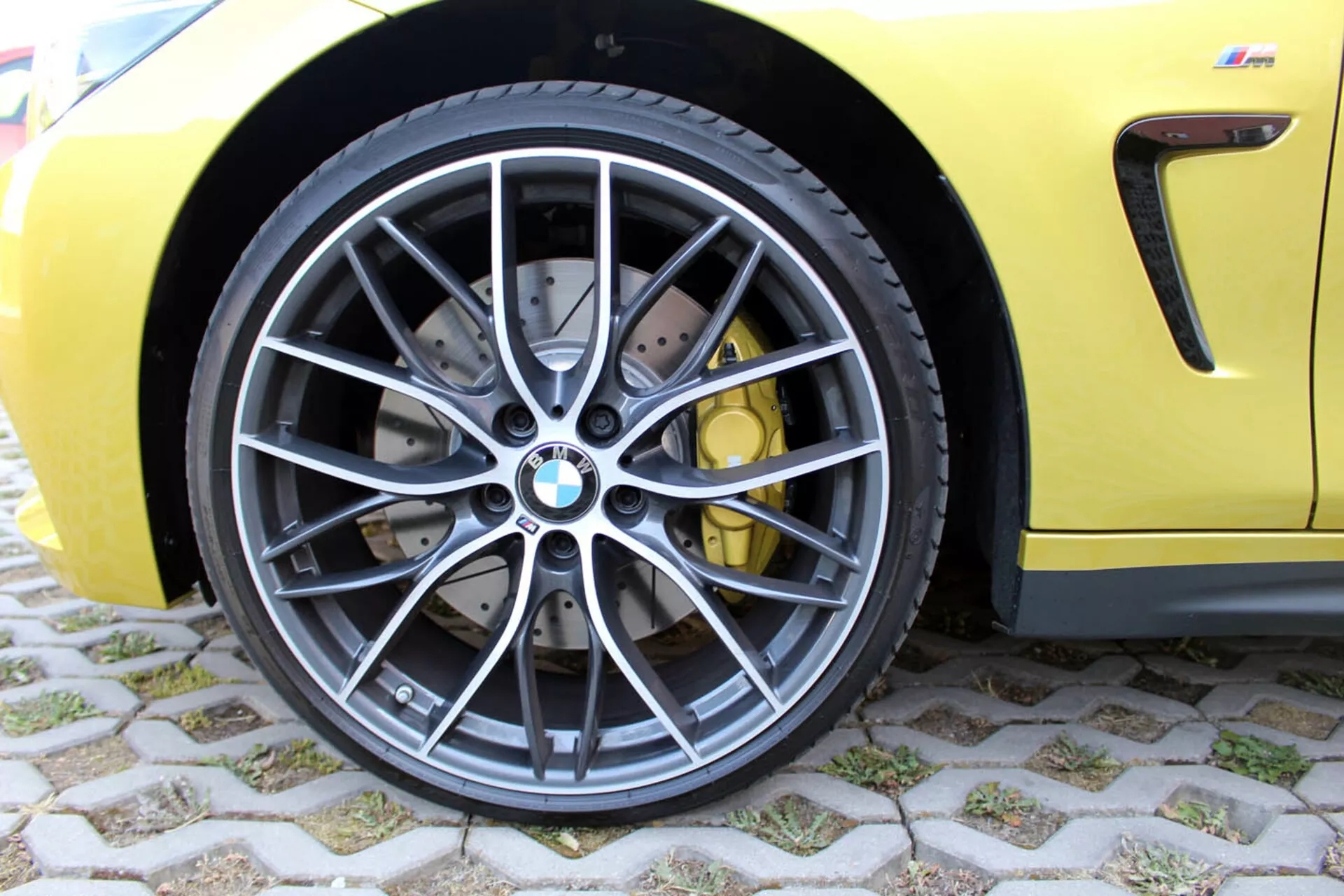 Vista ravvicinata della ruota anteriore BMW Serie 4 Coupé 2013 con design a razze in lega grigio scuro, pneumatico radiale tubeless a basso profilo, sistema frenante ad alte prestazioni con dischi forati e pinze gialle, su una carrozzeria gialla sportiva