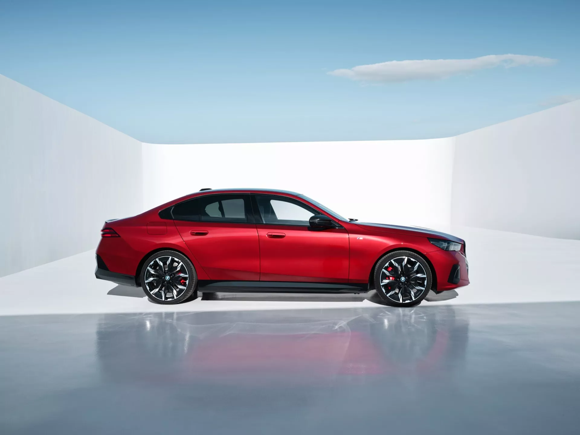 Berlina rossa a quattro porte BMW Serie 5 (G60-G61) in ambientazione studio con pavimento riflettente, che mostra profilo laterale, design moderno e funzionalità avanzate